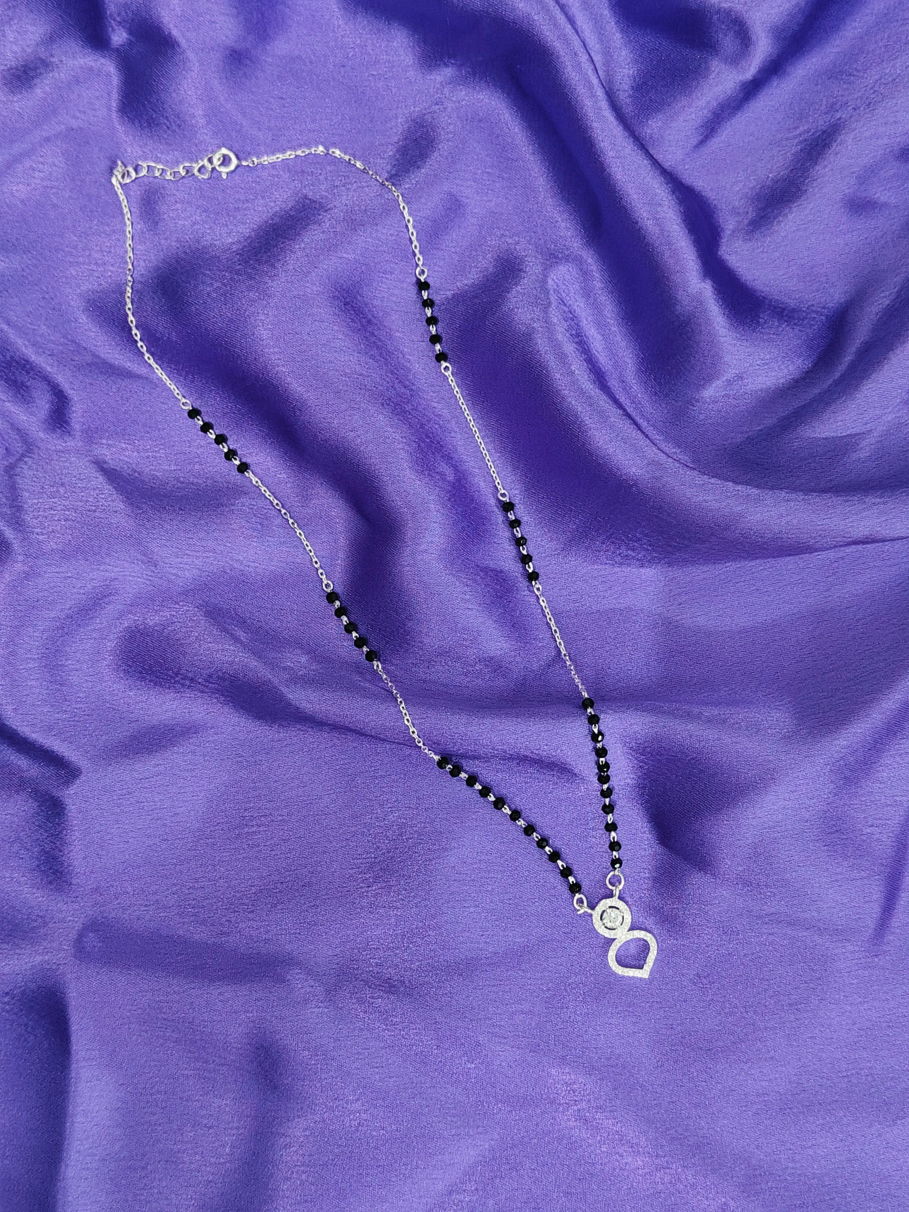 Necklace with black beads and a silver clasp on a purple fabric background