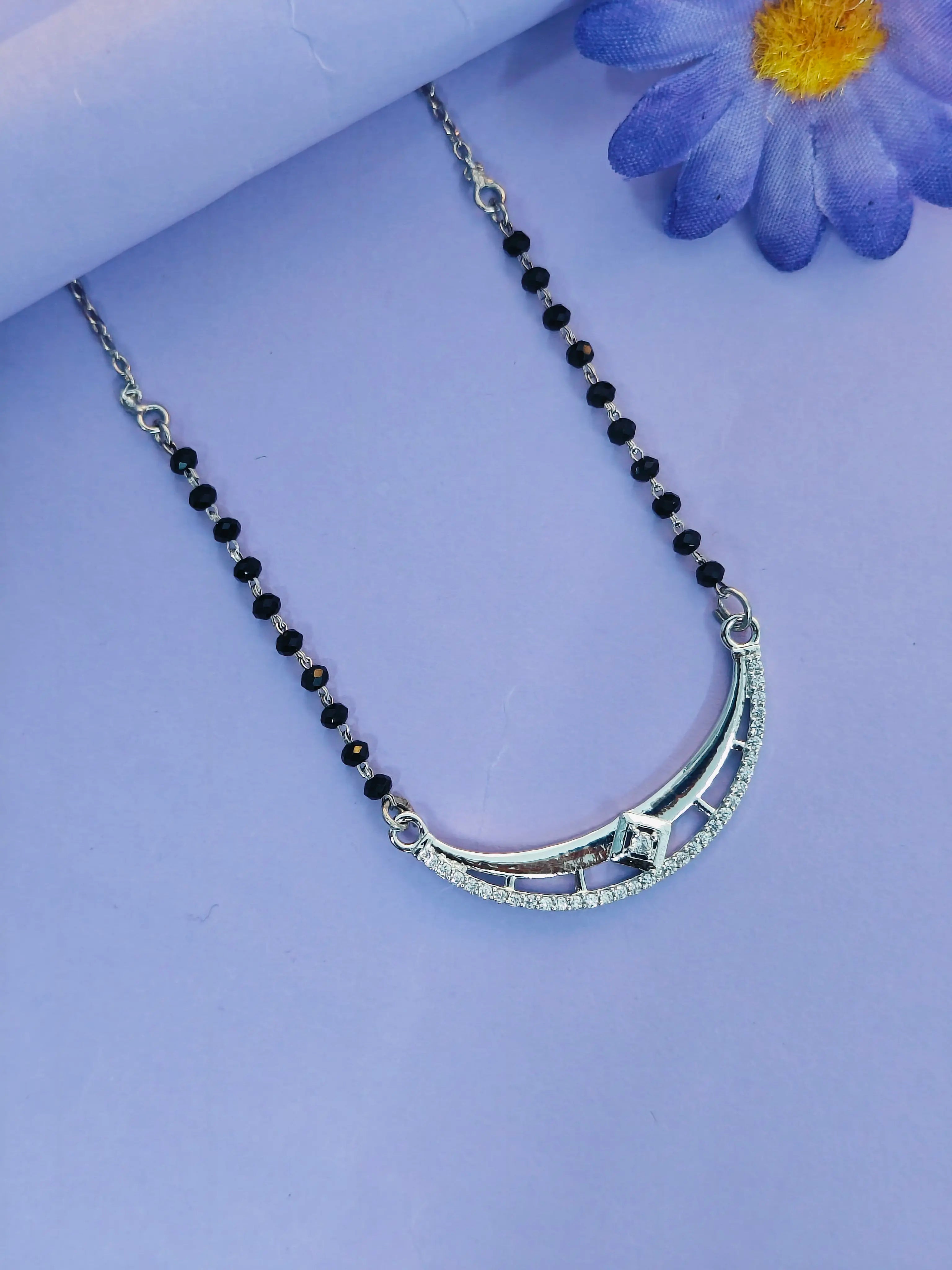 Silver necklace with black beads on a purple background with a blue flower.