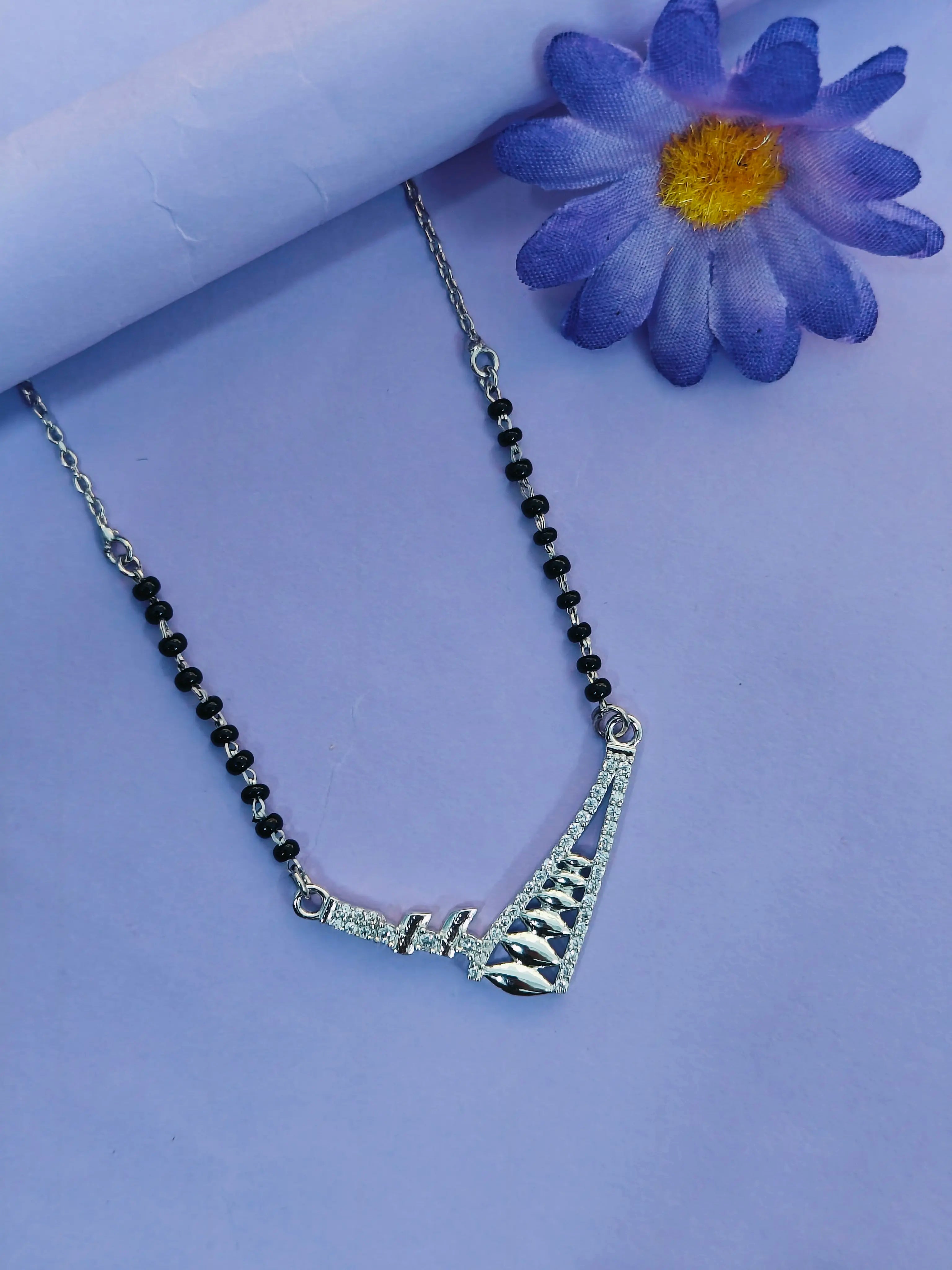 Necklace with black beads and silver clasp on a light purple background with a blue flower.