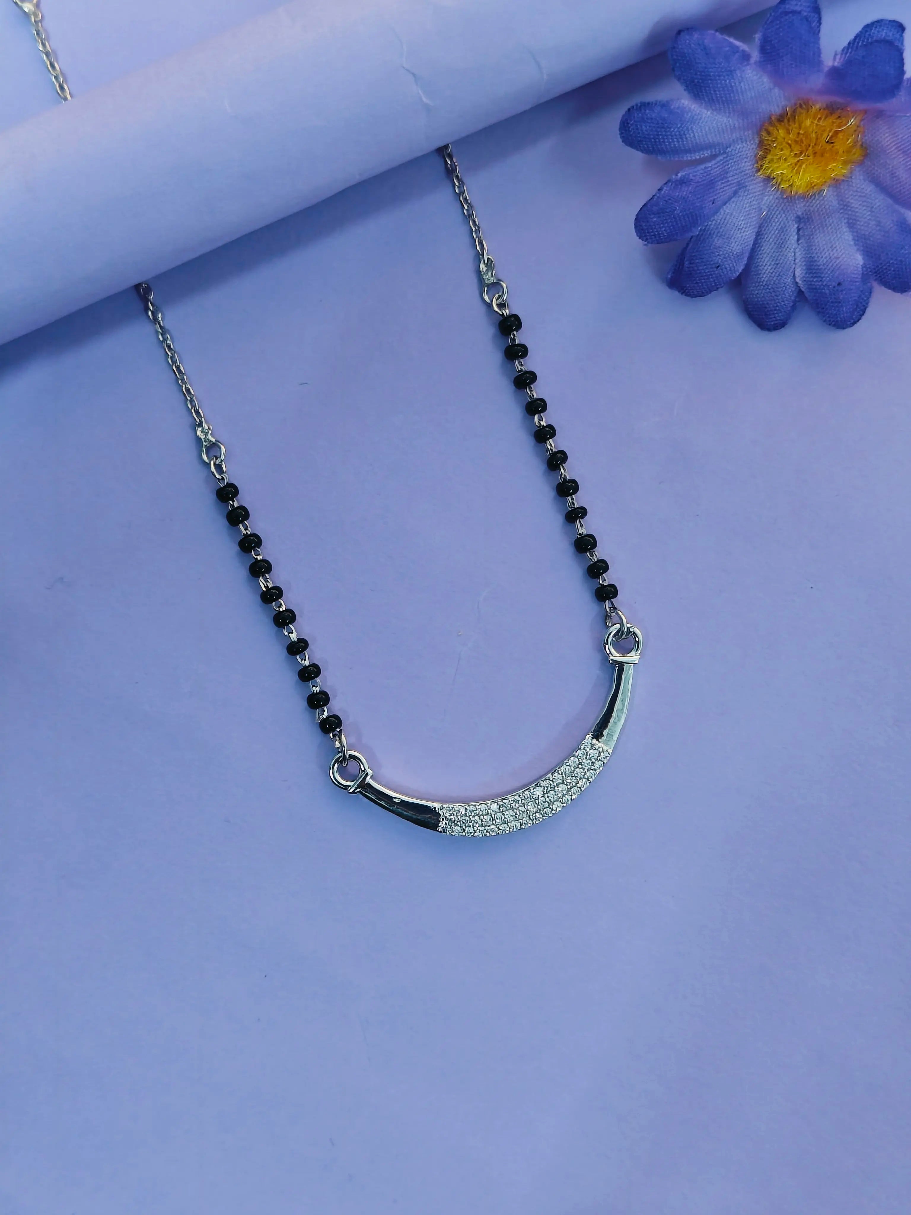 Necklace with black beads and silver crescent moon pendant on a purple background with a flower.