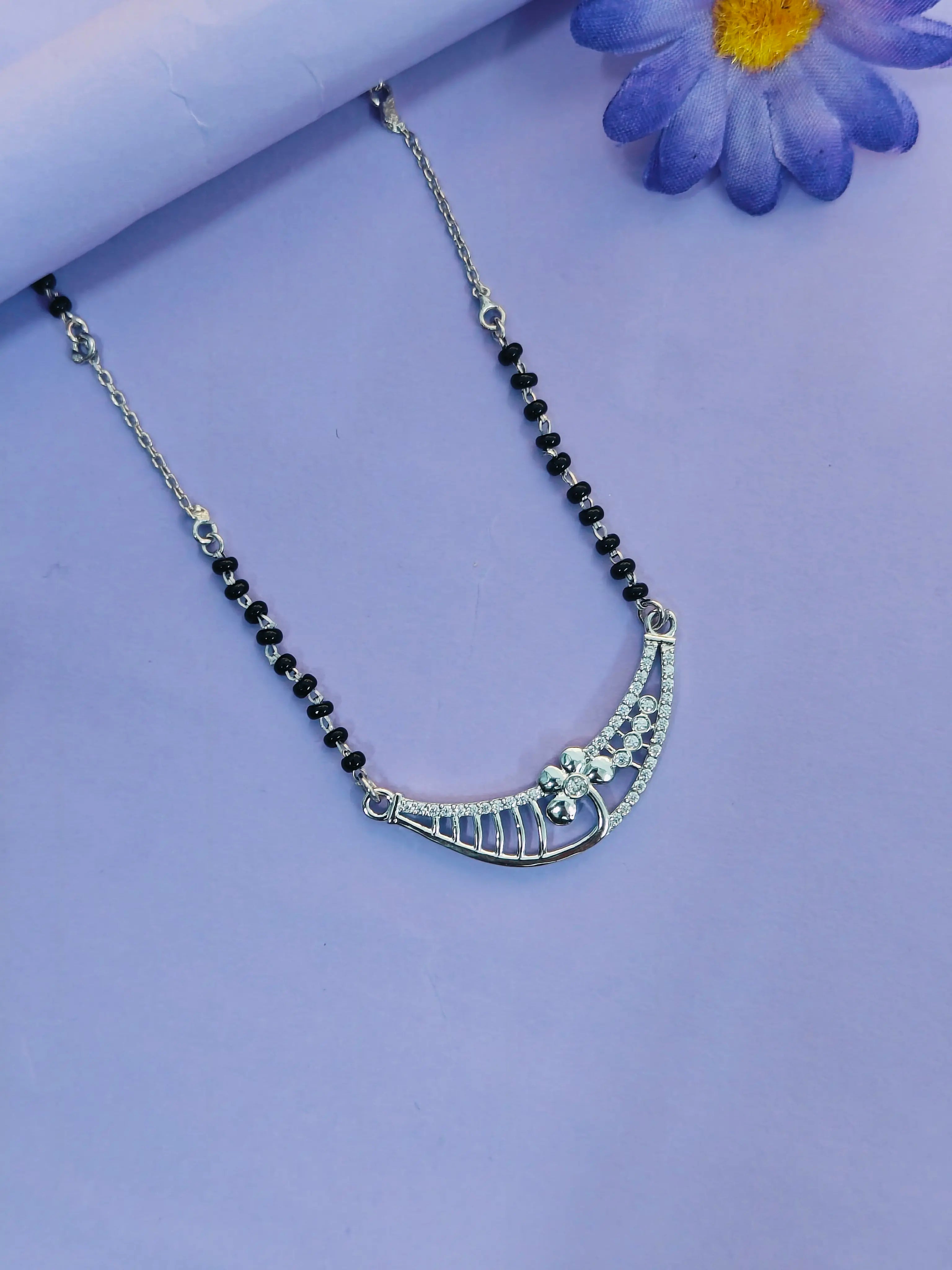 Necklace with black beads and silver pendant on a light purple background