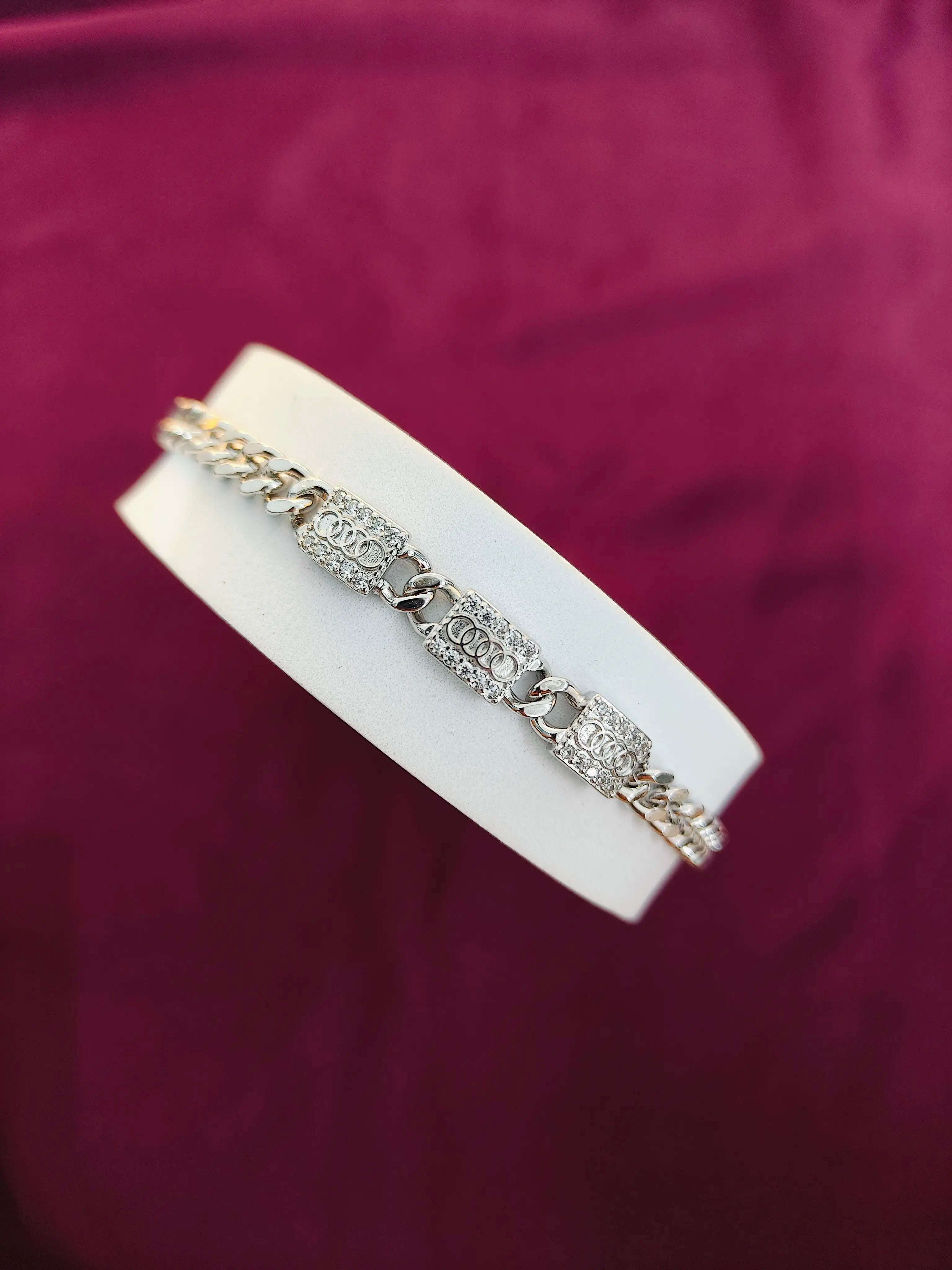 Silver bracelet on a white stand against a purple background