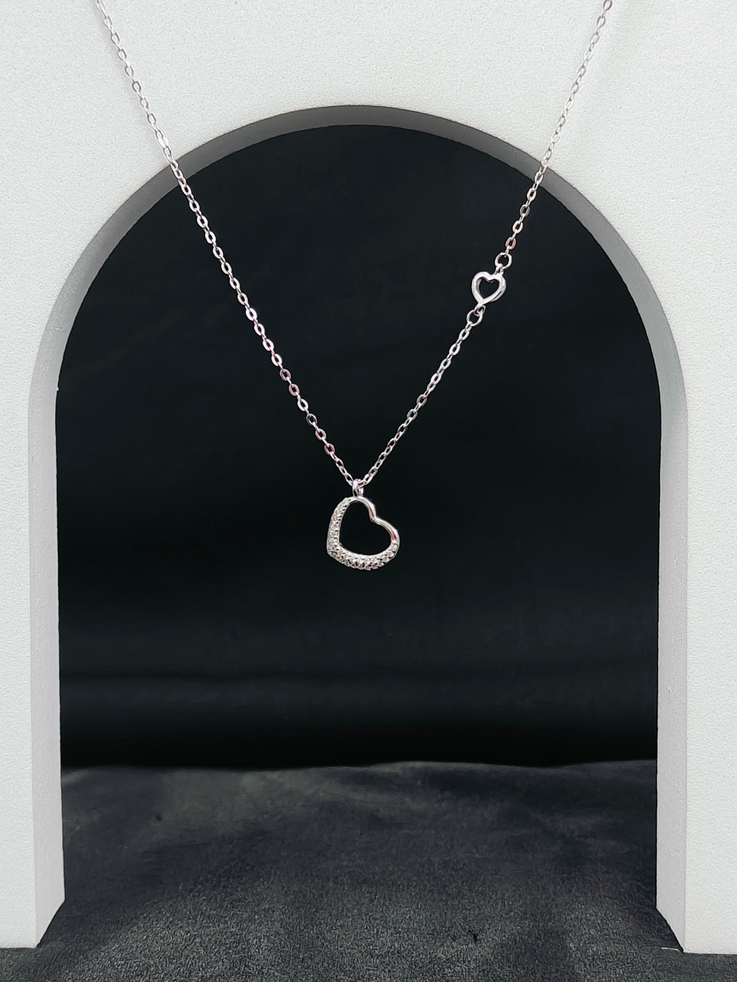 Silver heart-shaped necklace hanging against a black background