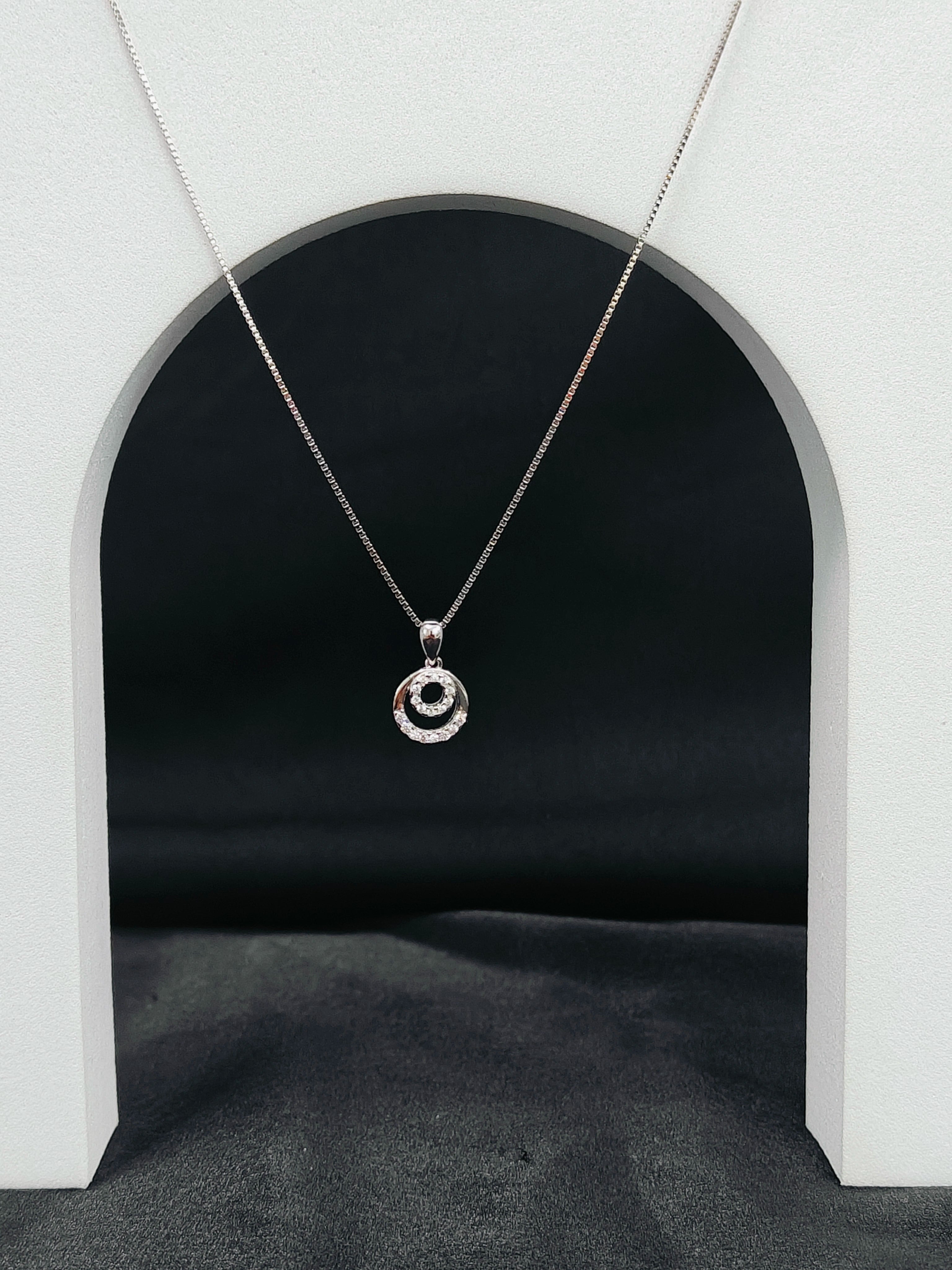 Necklace with a circular pendant hanging in front of a black archway.