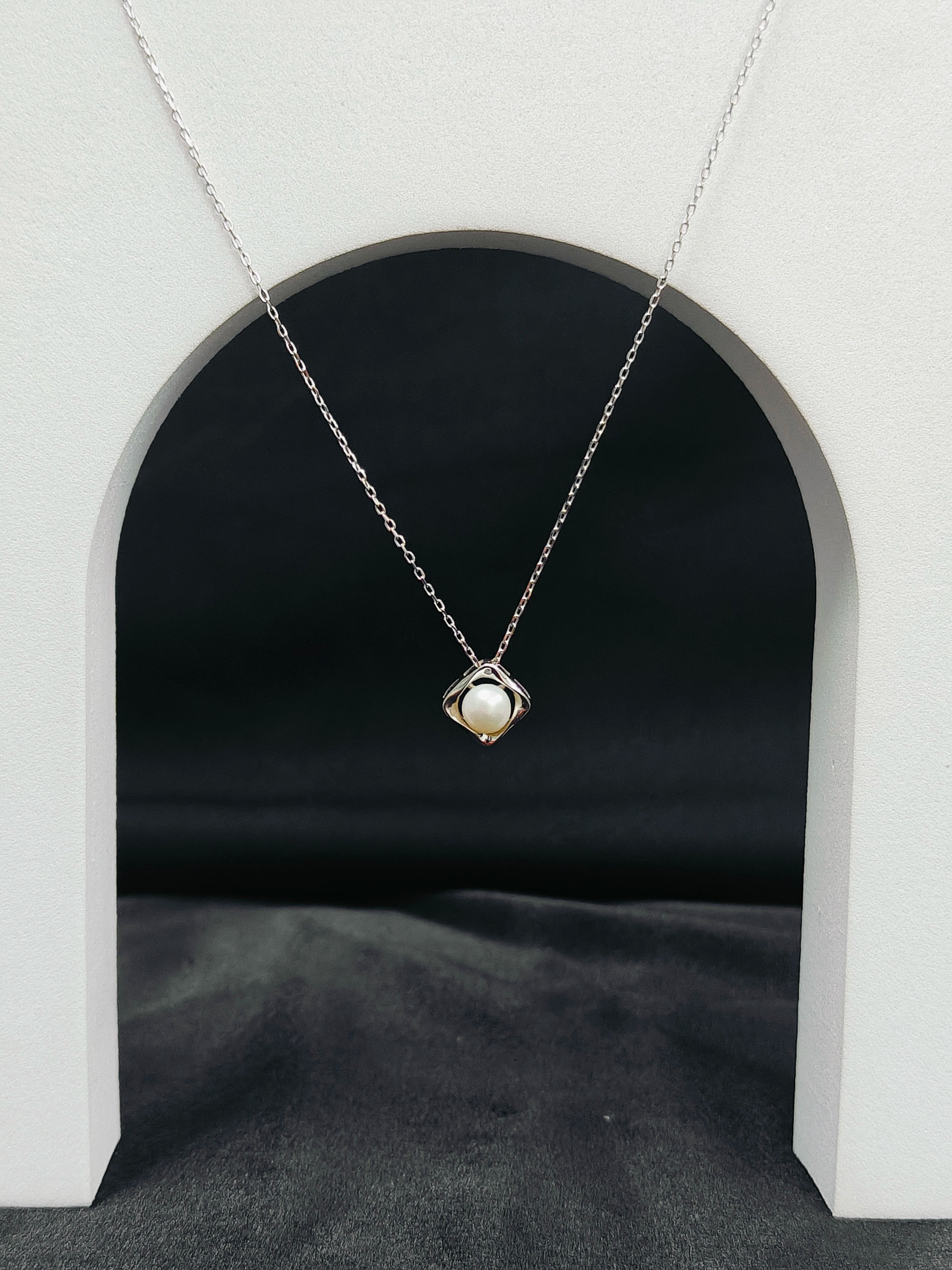 Necklace with a pendant hanging in front of a black archway on a gray surface.