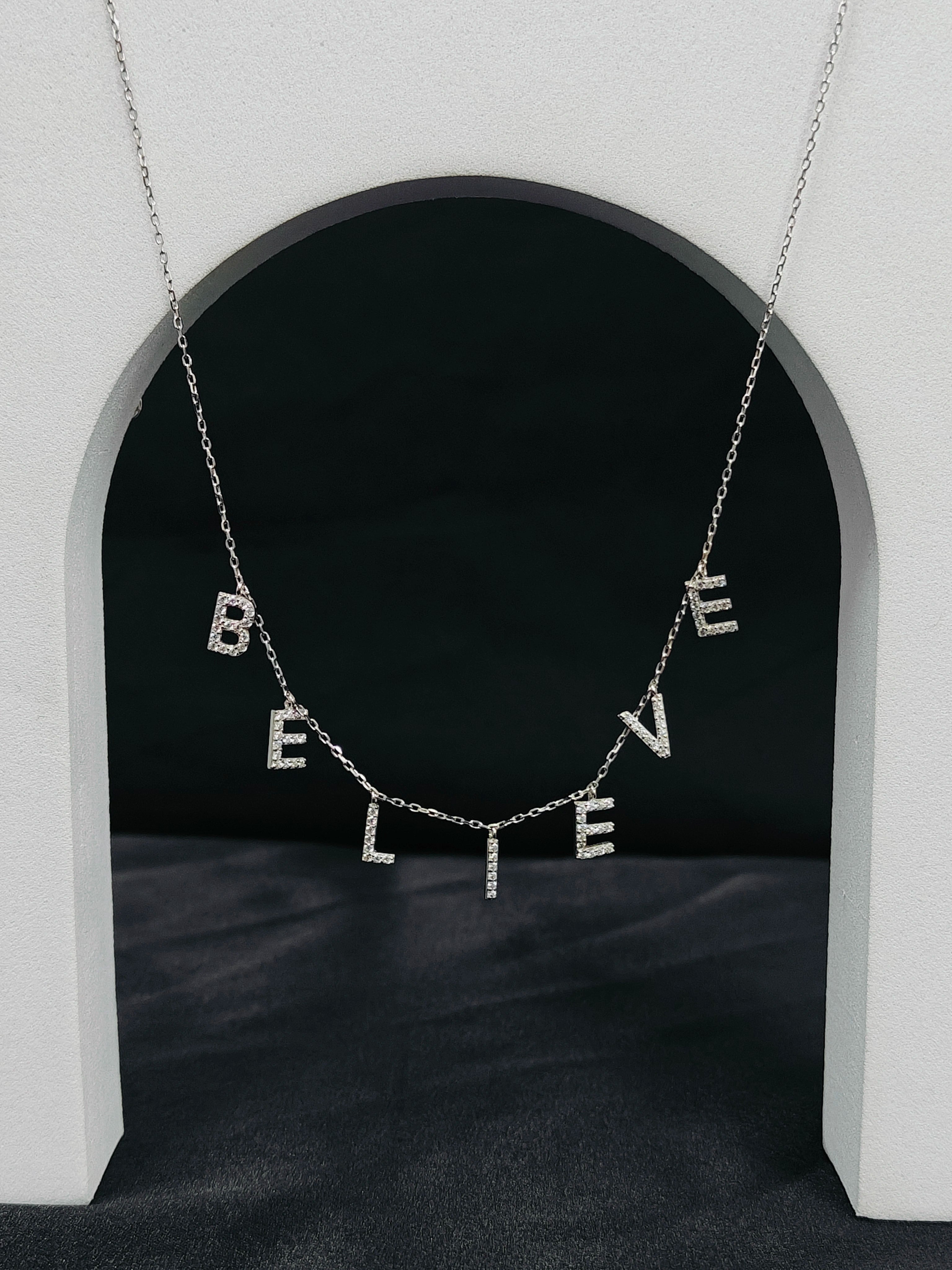 Necklace with 'BELIEVE' letters hanging in front of a black archway.