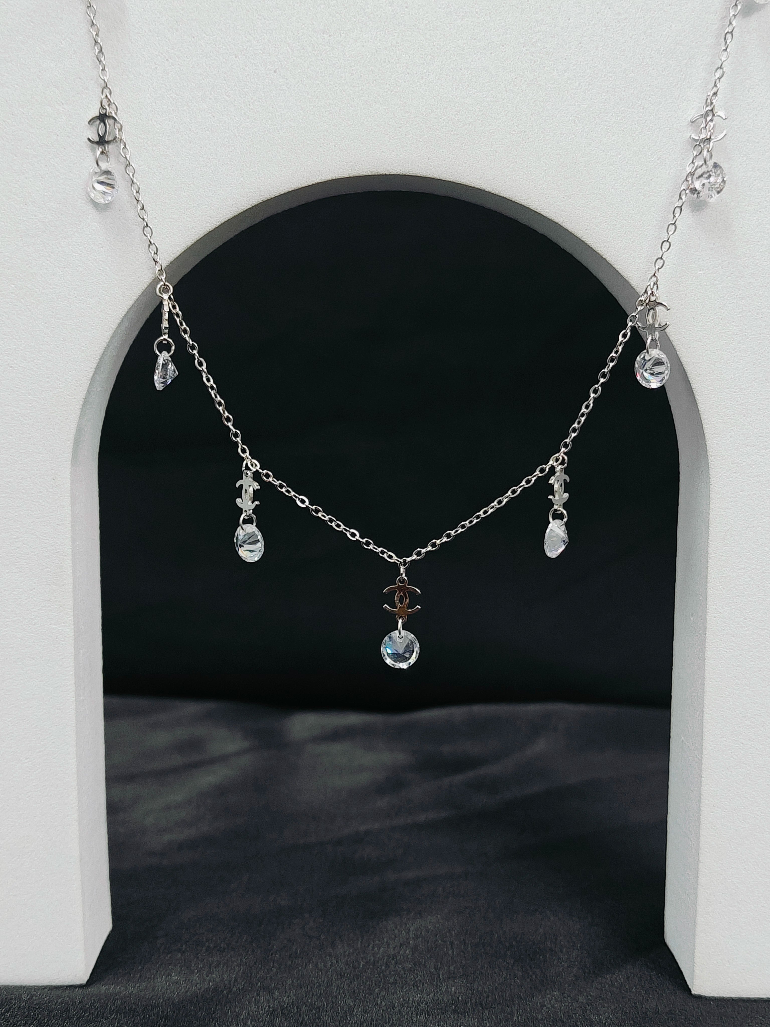 Delicate silver necklace with small pendants on a white archway background