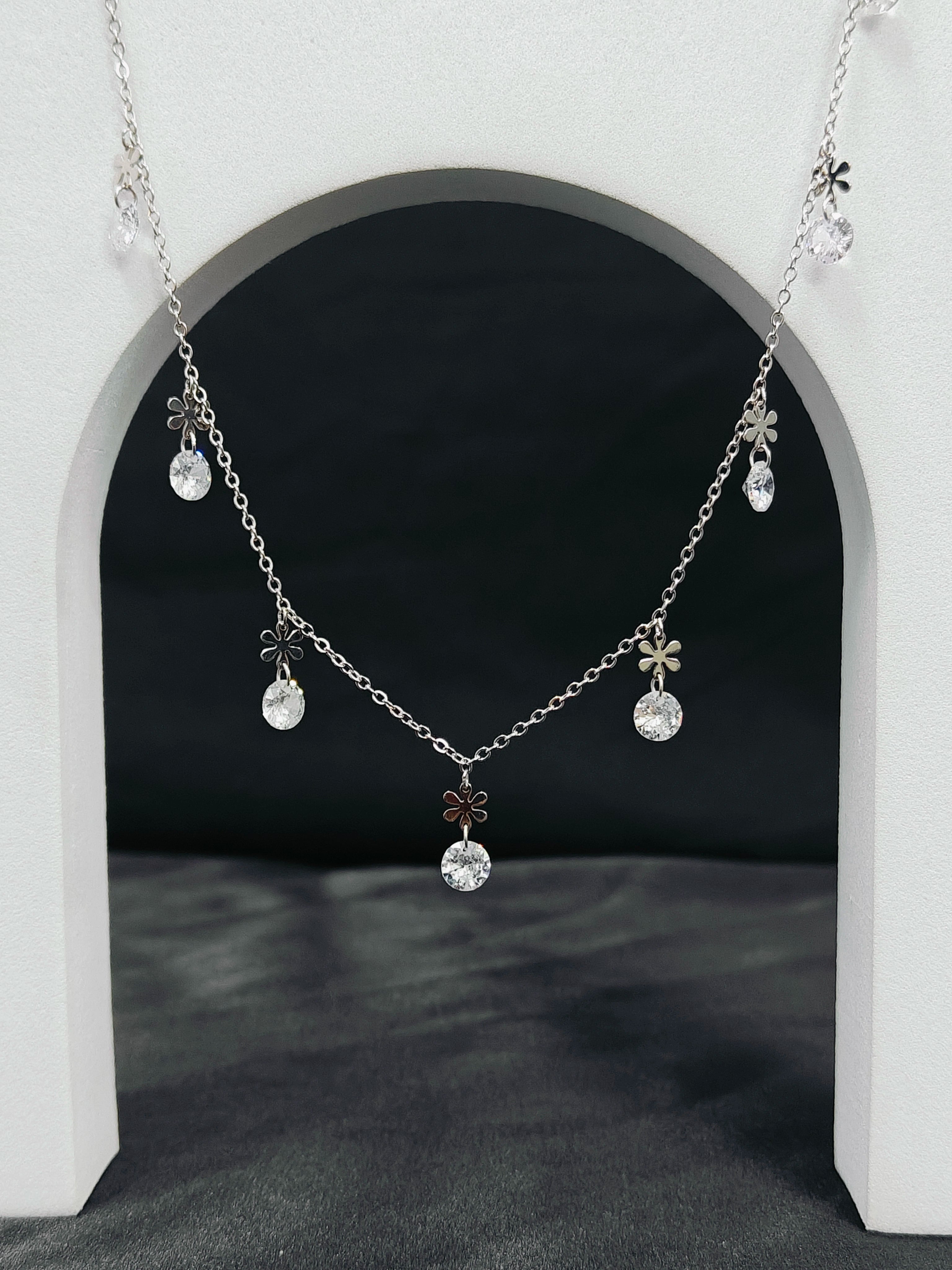 Silver necklace with floral and crystal pendants hanging against a black background