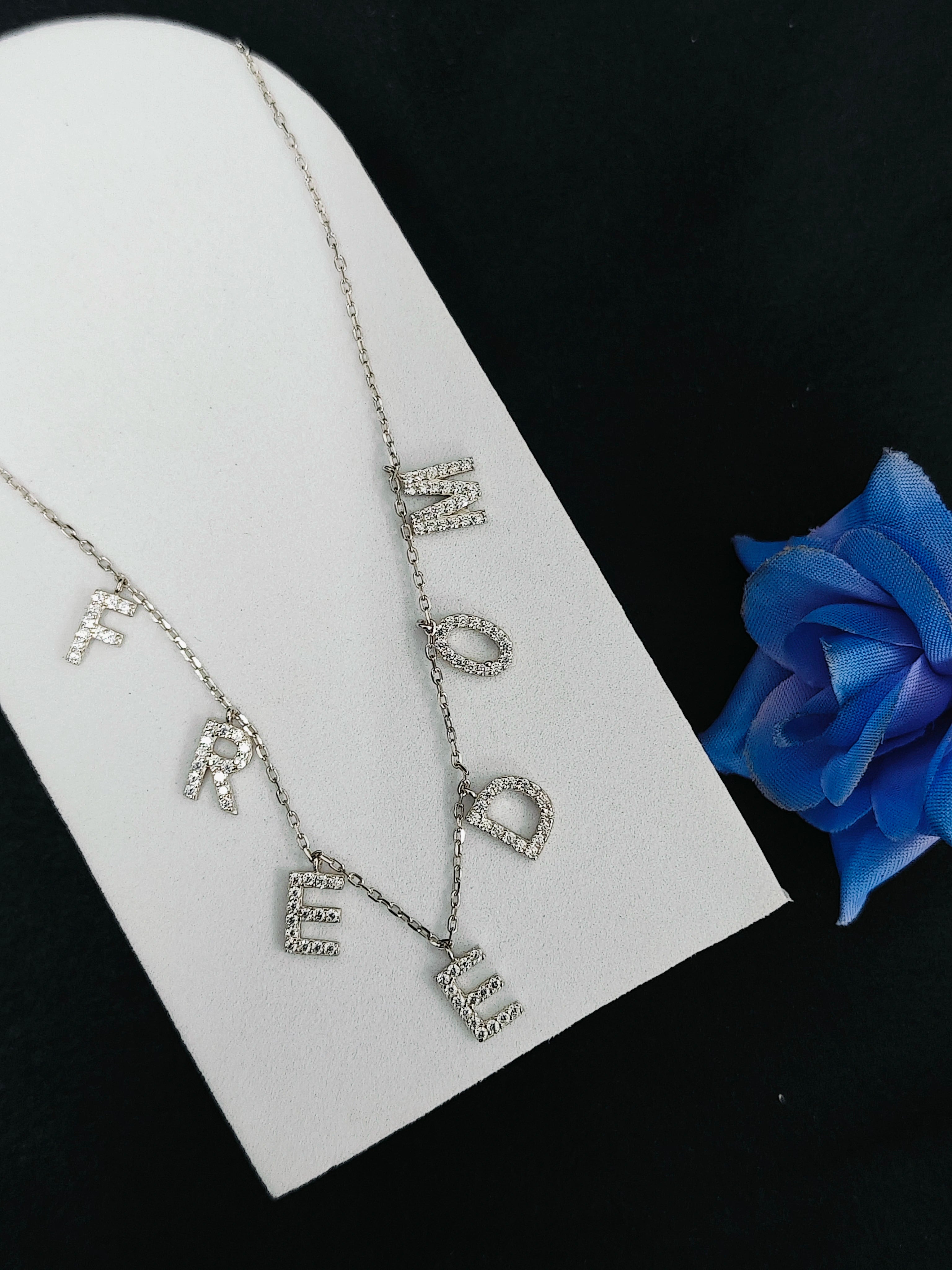 Silver necklace with 'LOVE' pendant on a white stand with a blue flower.