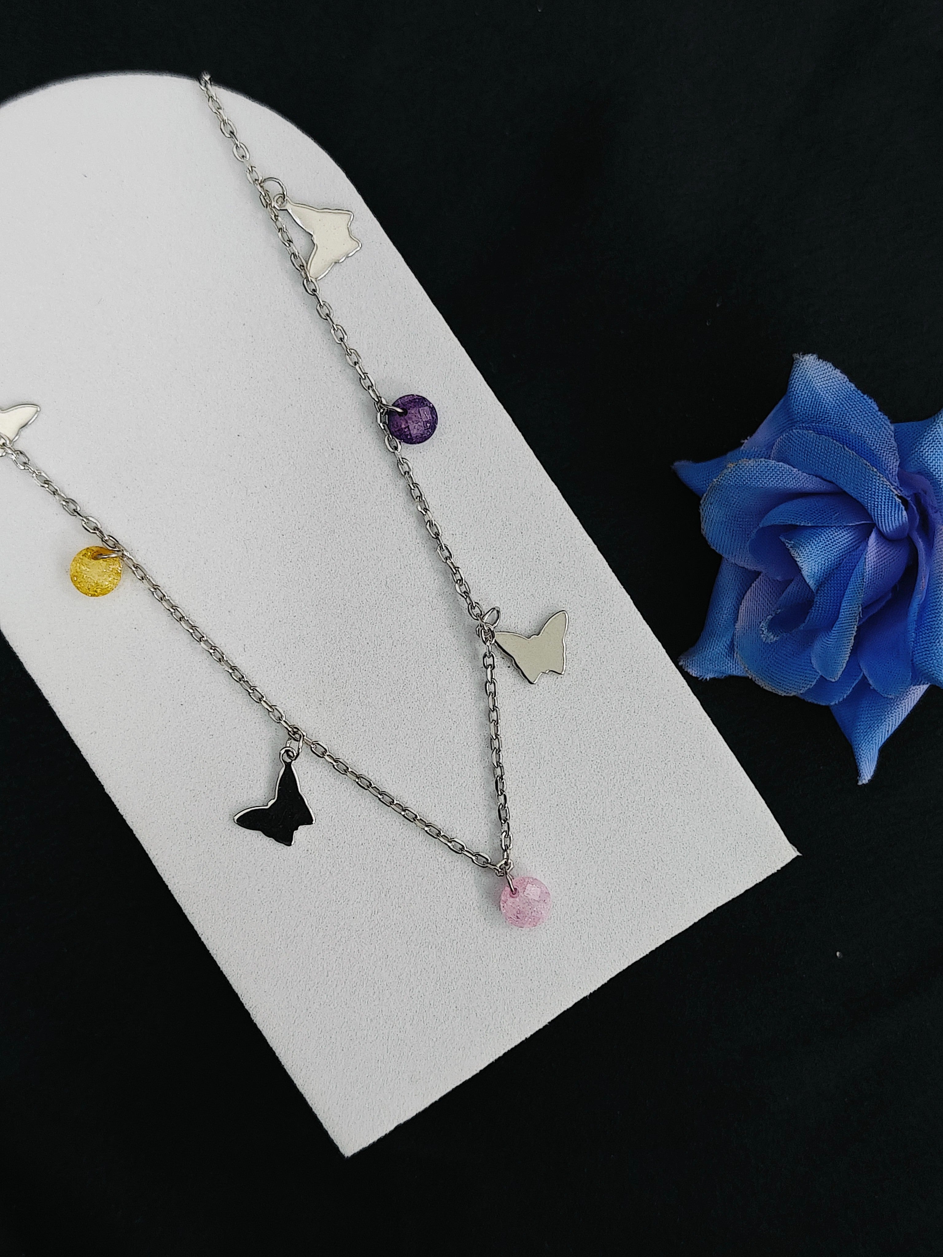 Necklace with butterfly and colorful bead charms on a white card with a blue flower.