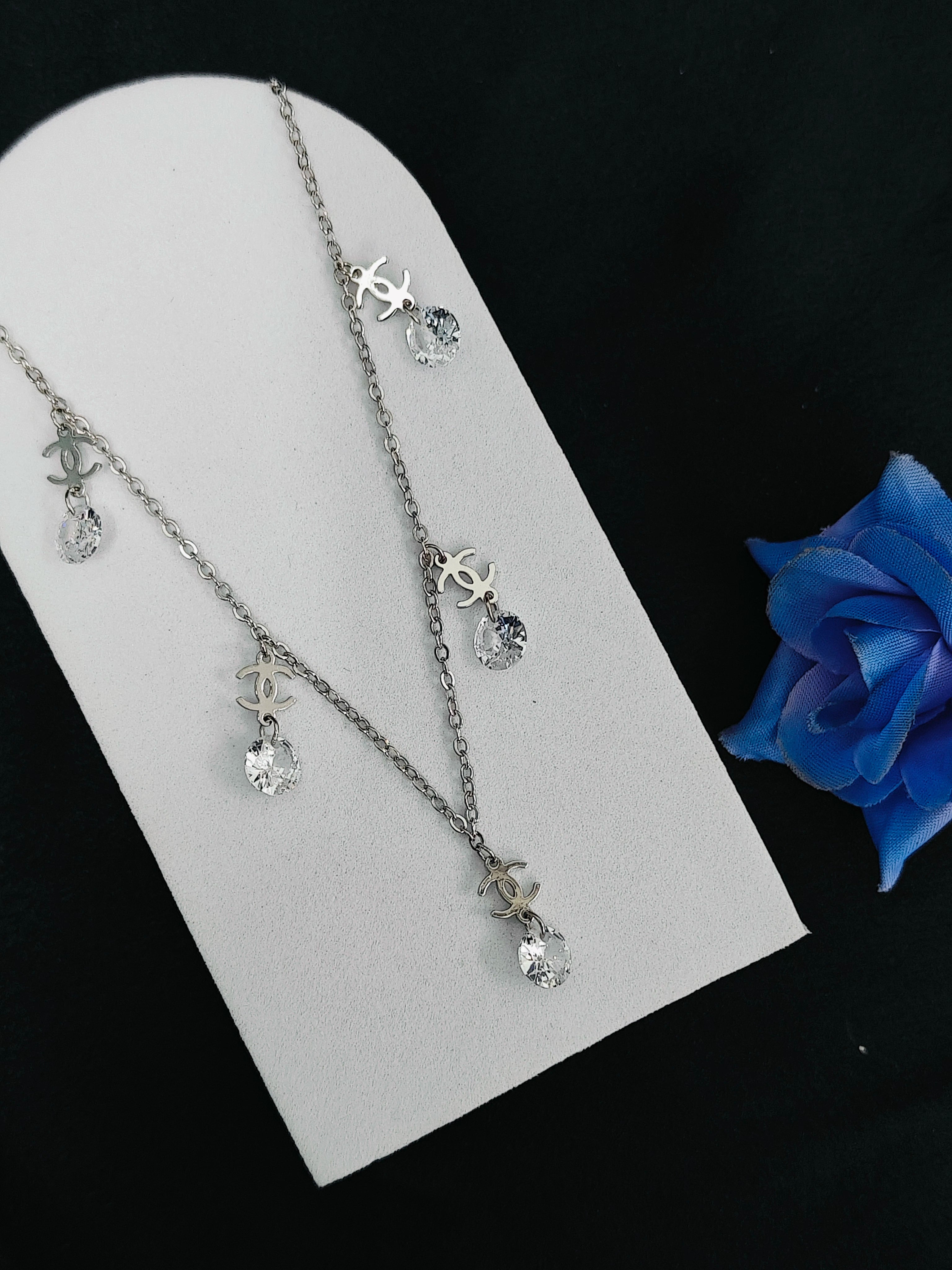 Silver necklace with crystal pendants on a white stand with a blue rose.