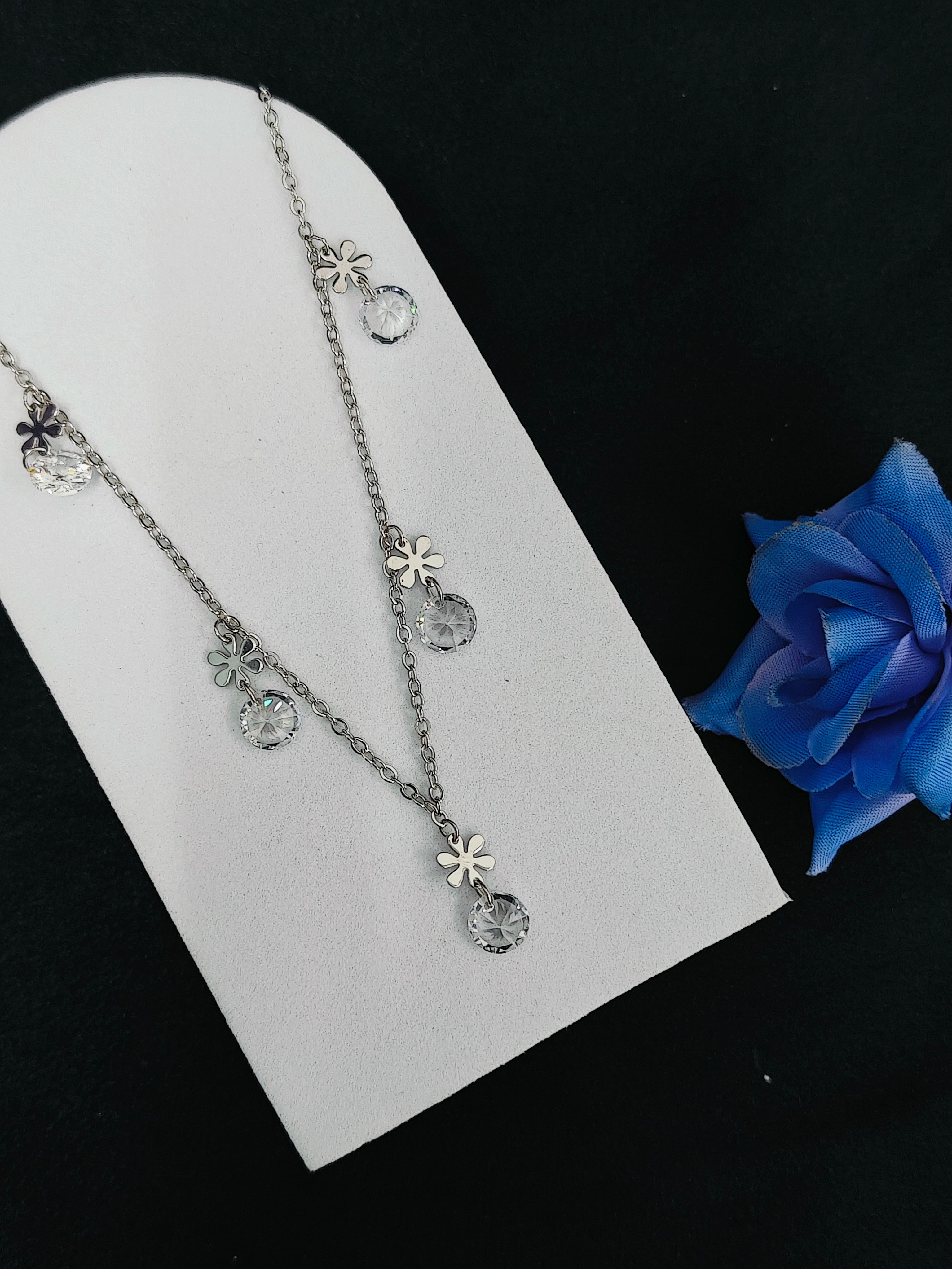 Silver necklace with floral pendants on a white card with a blue flower in the background