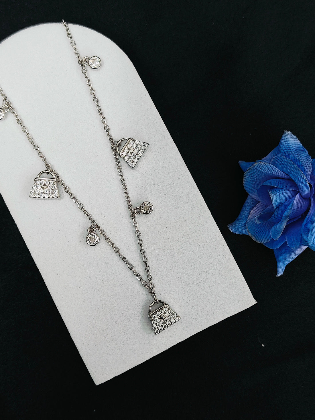 Silver necklace with pendant charms on a white card, blue rose at the bottom.