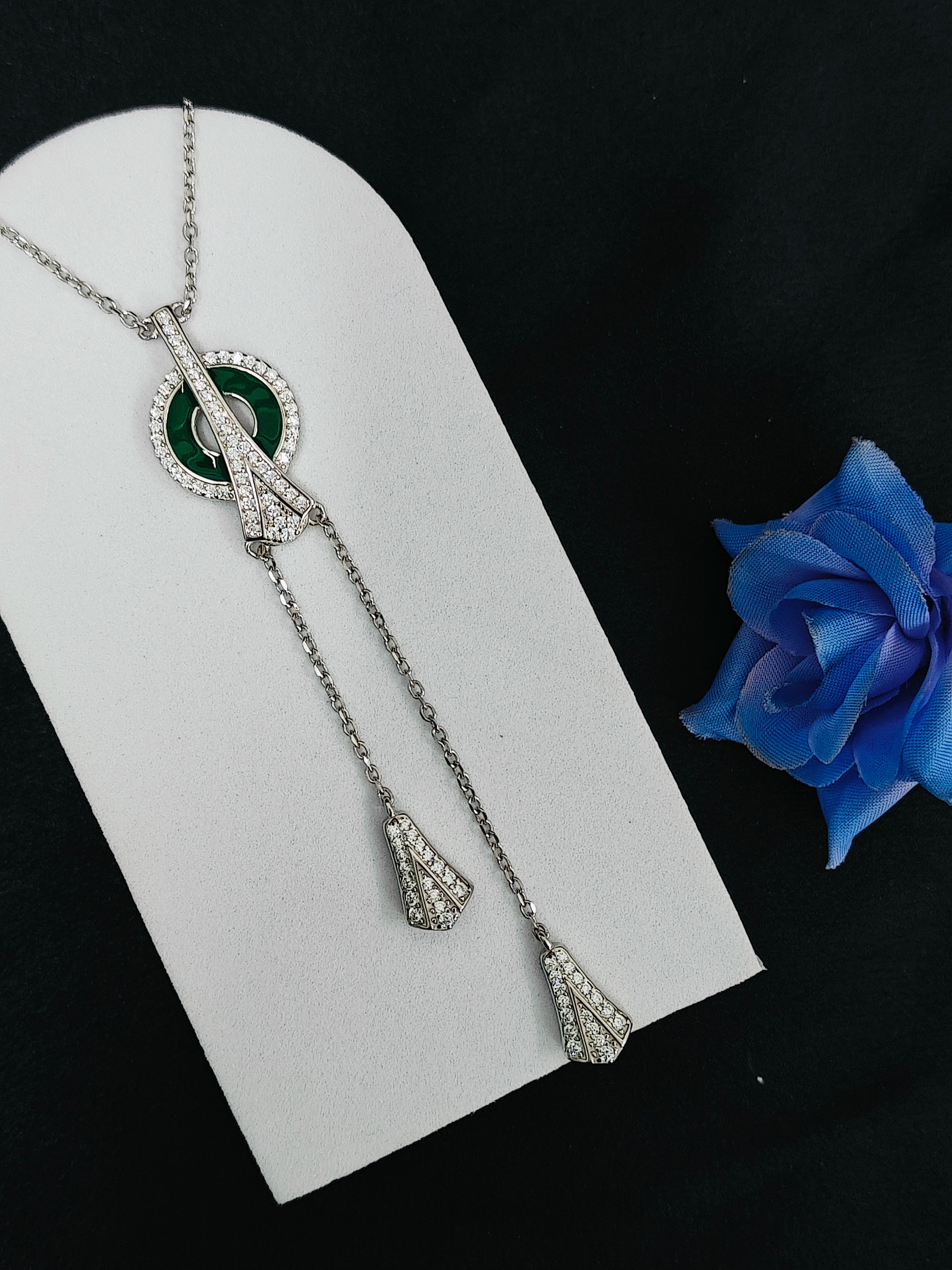 Silver necklace with green gemstone on a white card with a blue flower in the background