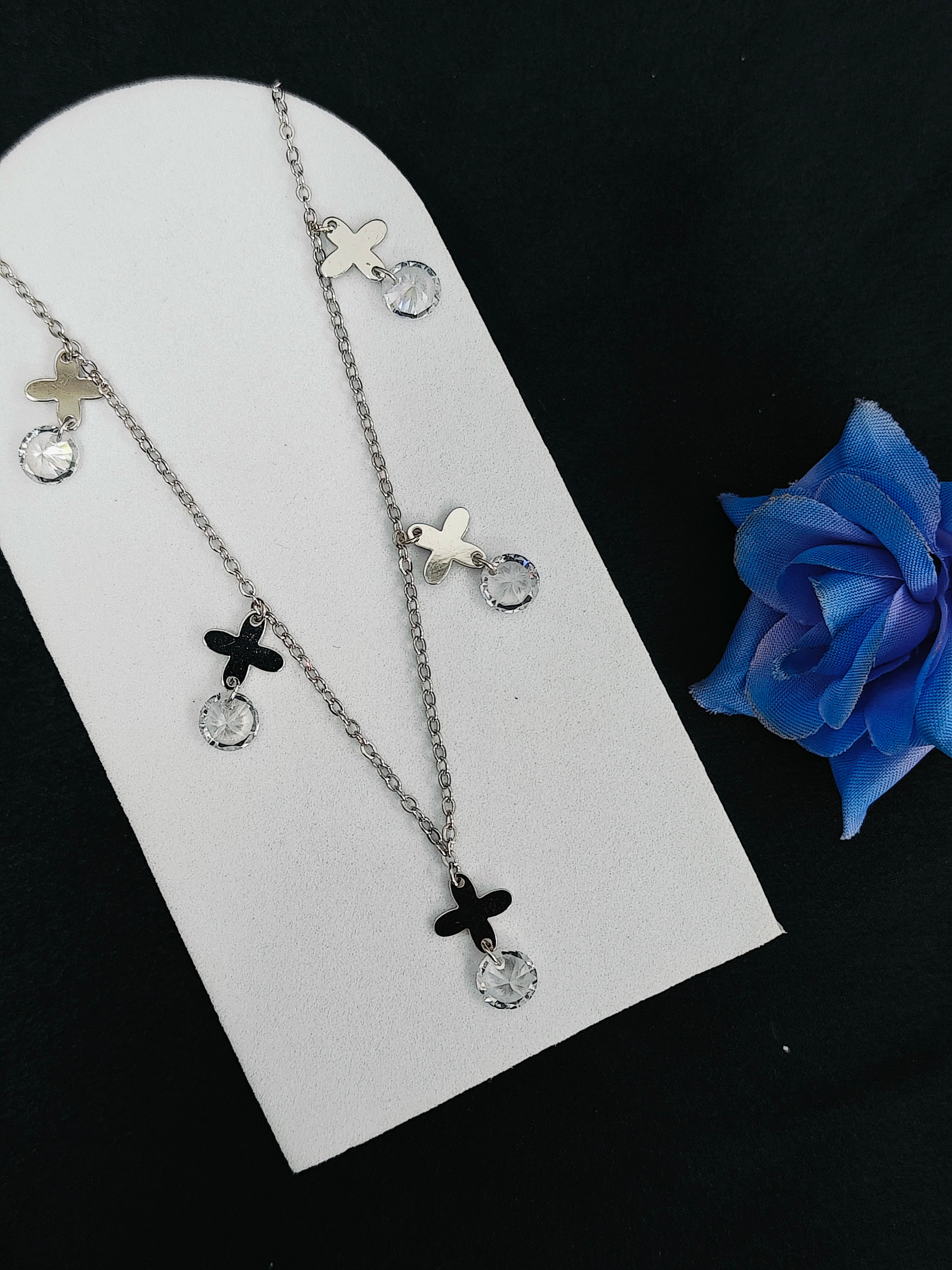 Necklace with cross and star pendants on a white card with a blue rose.