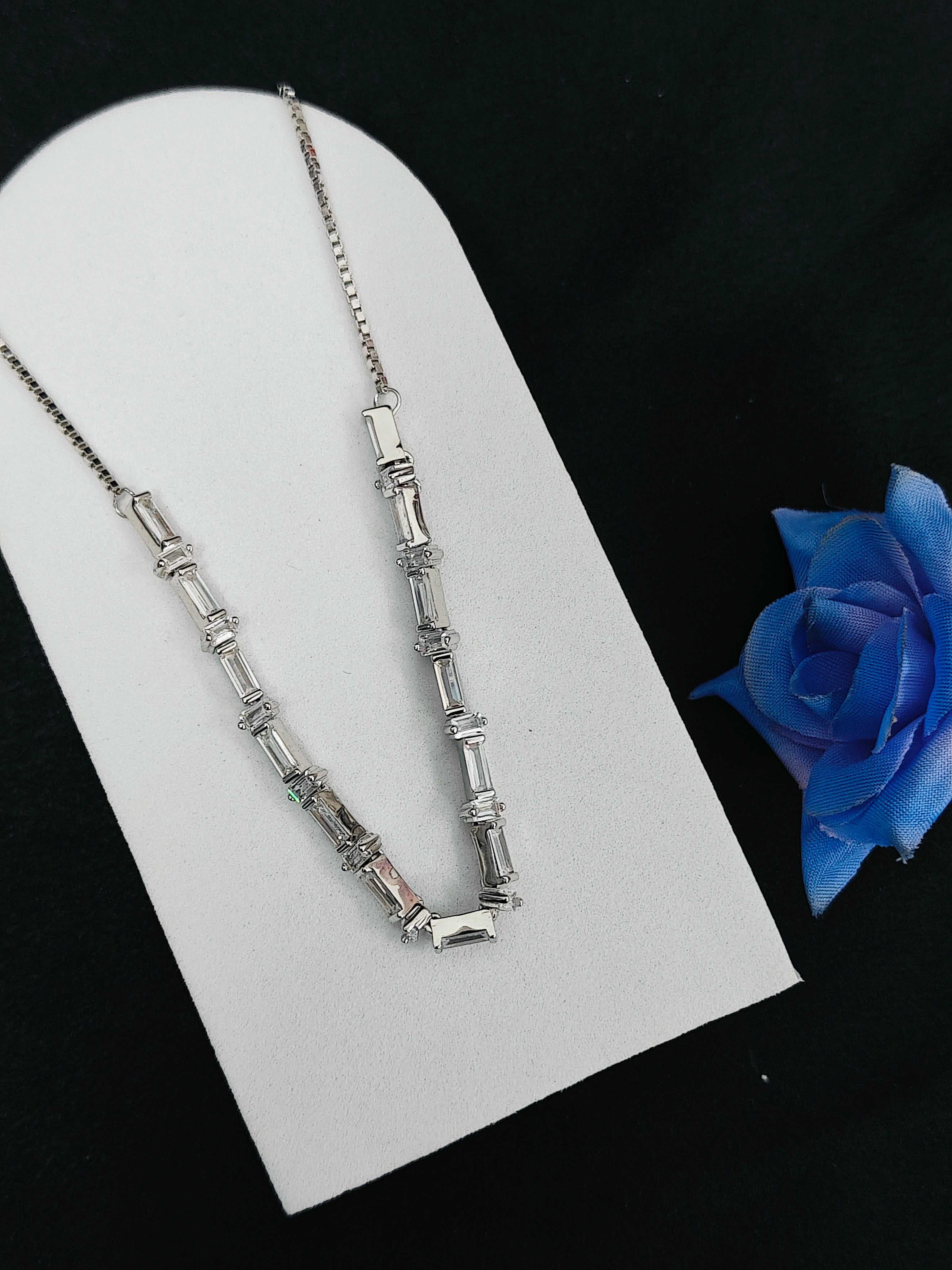 Silver necklace on a white stand with a blue rose on a black background
