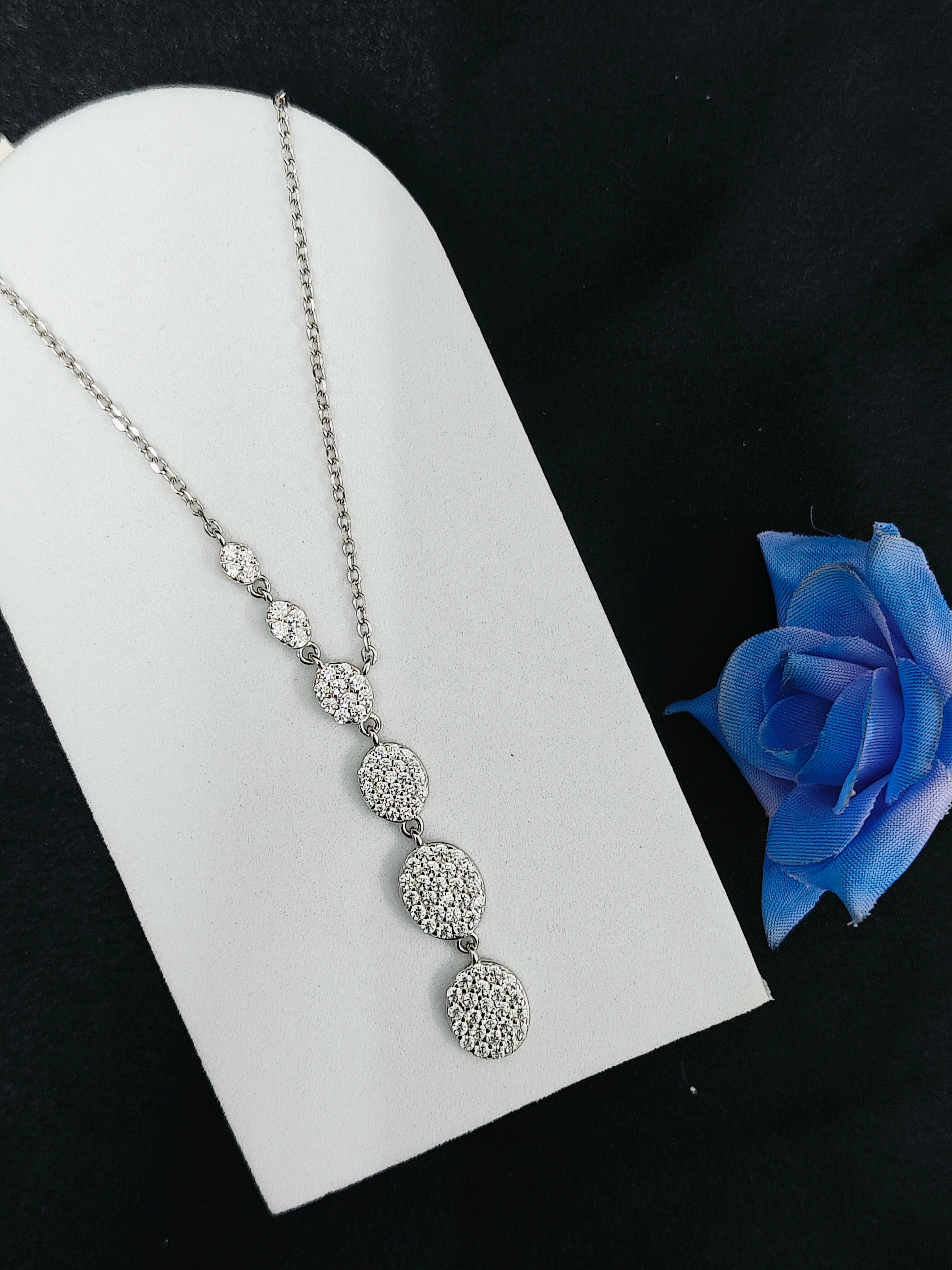 Silver necklace on a white stand with a blue rose on a black background