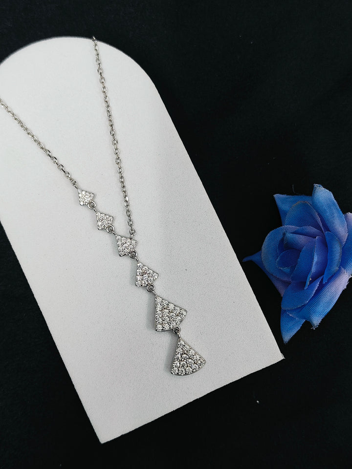 Silver necklace with diamond-like stones on a white stand with a blue flower.