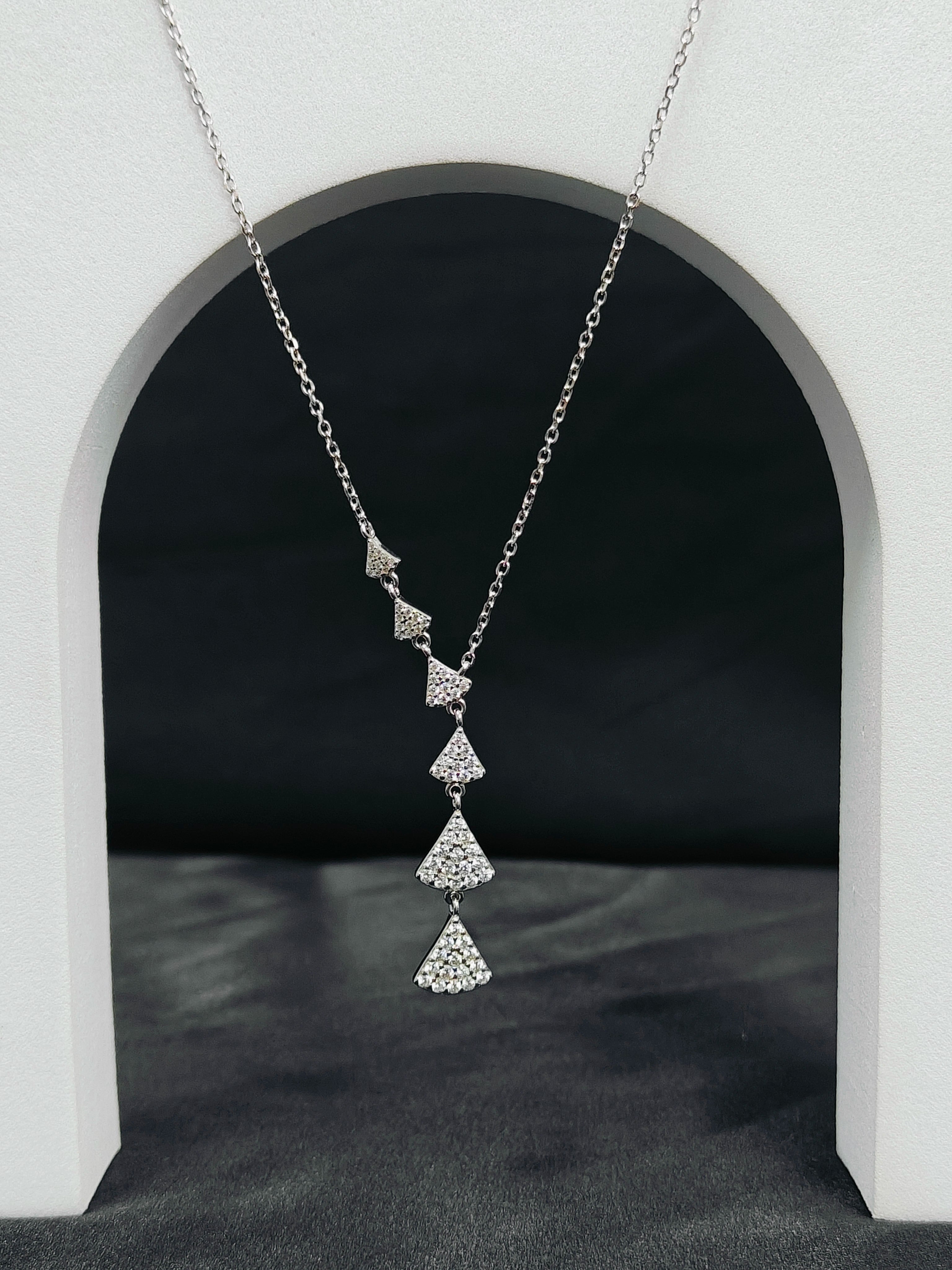 Silver necklace with diamond pendants hanging in front of a white archway.