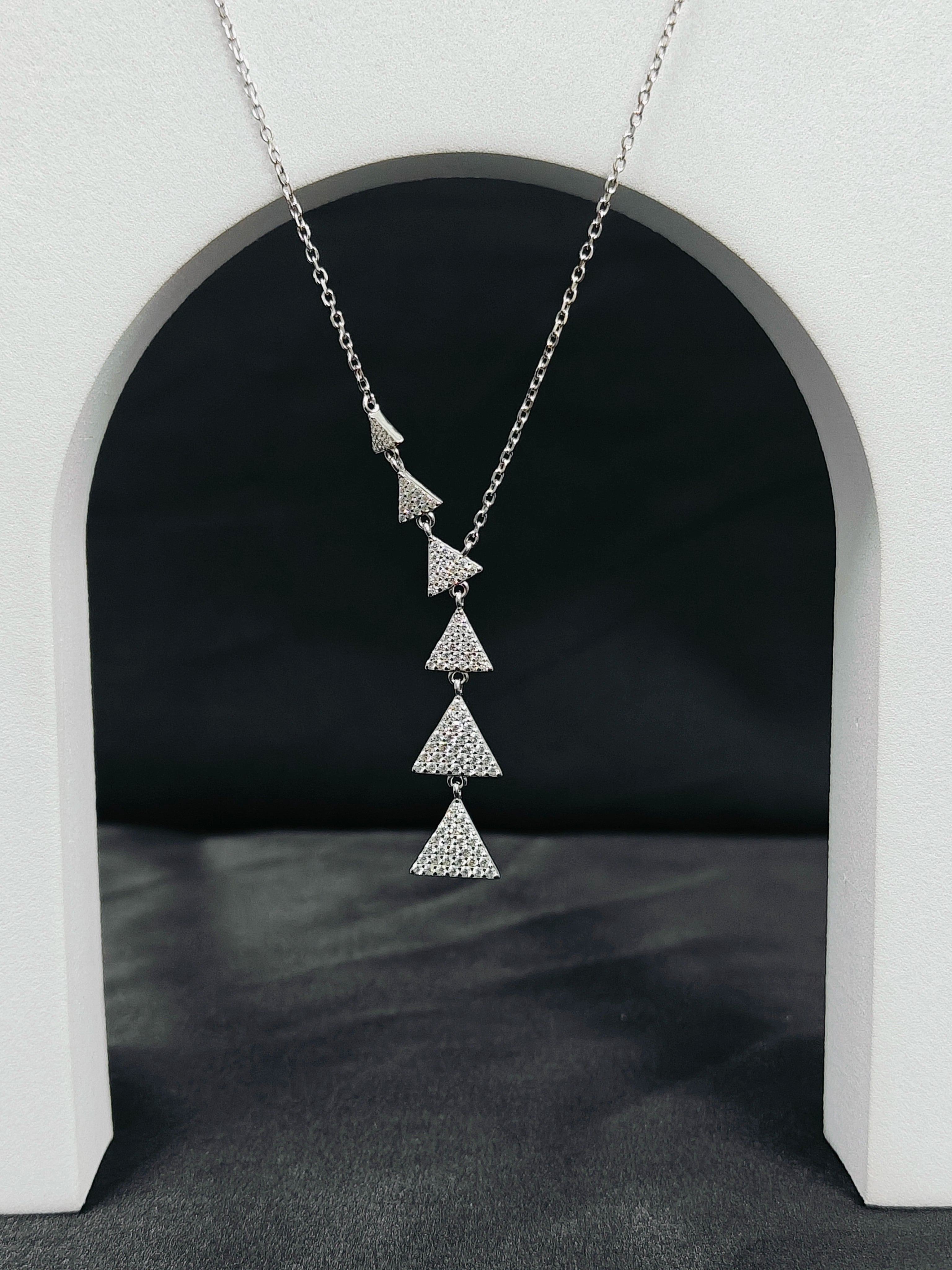 Silver necklace with triangular pendant on a dark background