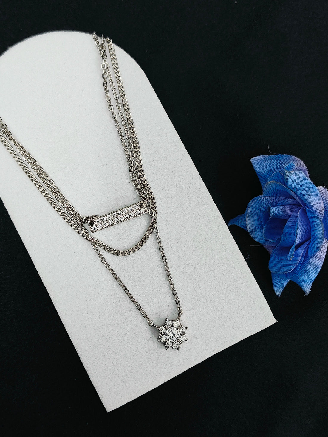 Silver necklace with a pendant on a white card with a blue rose below, against a black background
