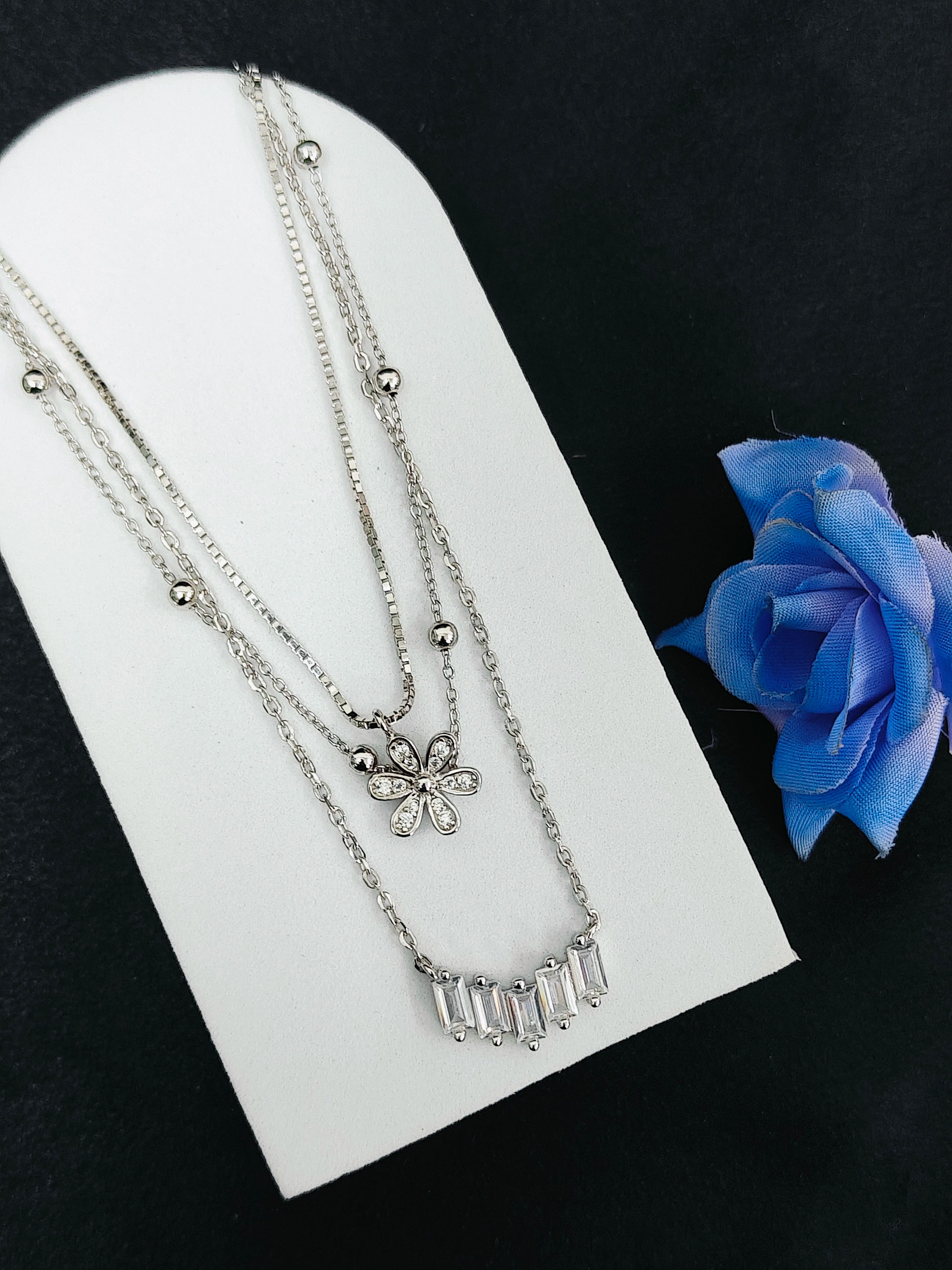 Silver necklaces on a white stand with a blue rose on a black background