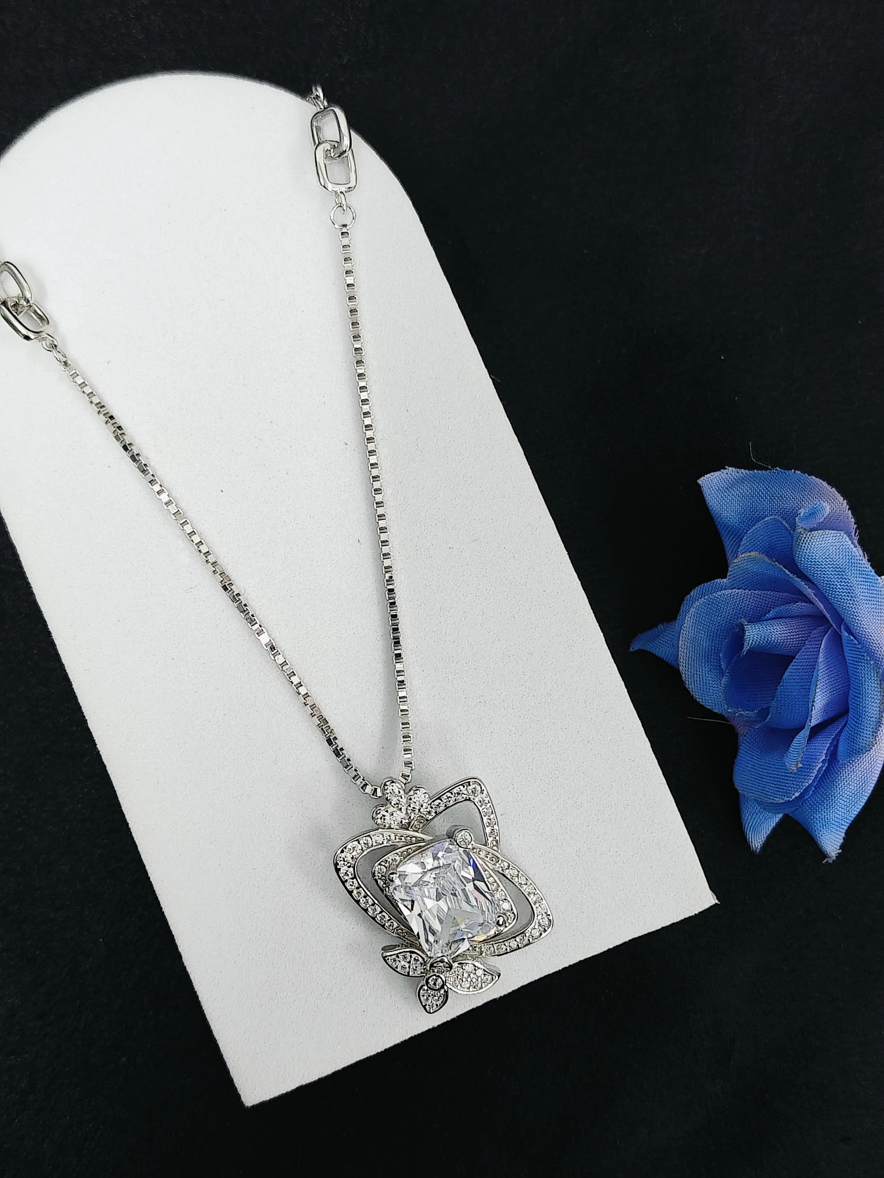 Silver necklace with a large diamond pendant on a white card with a blue rose.