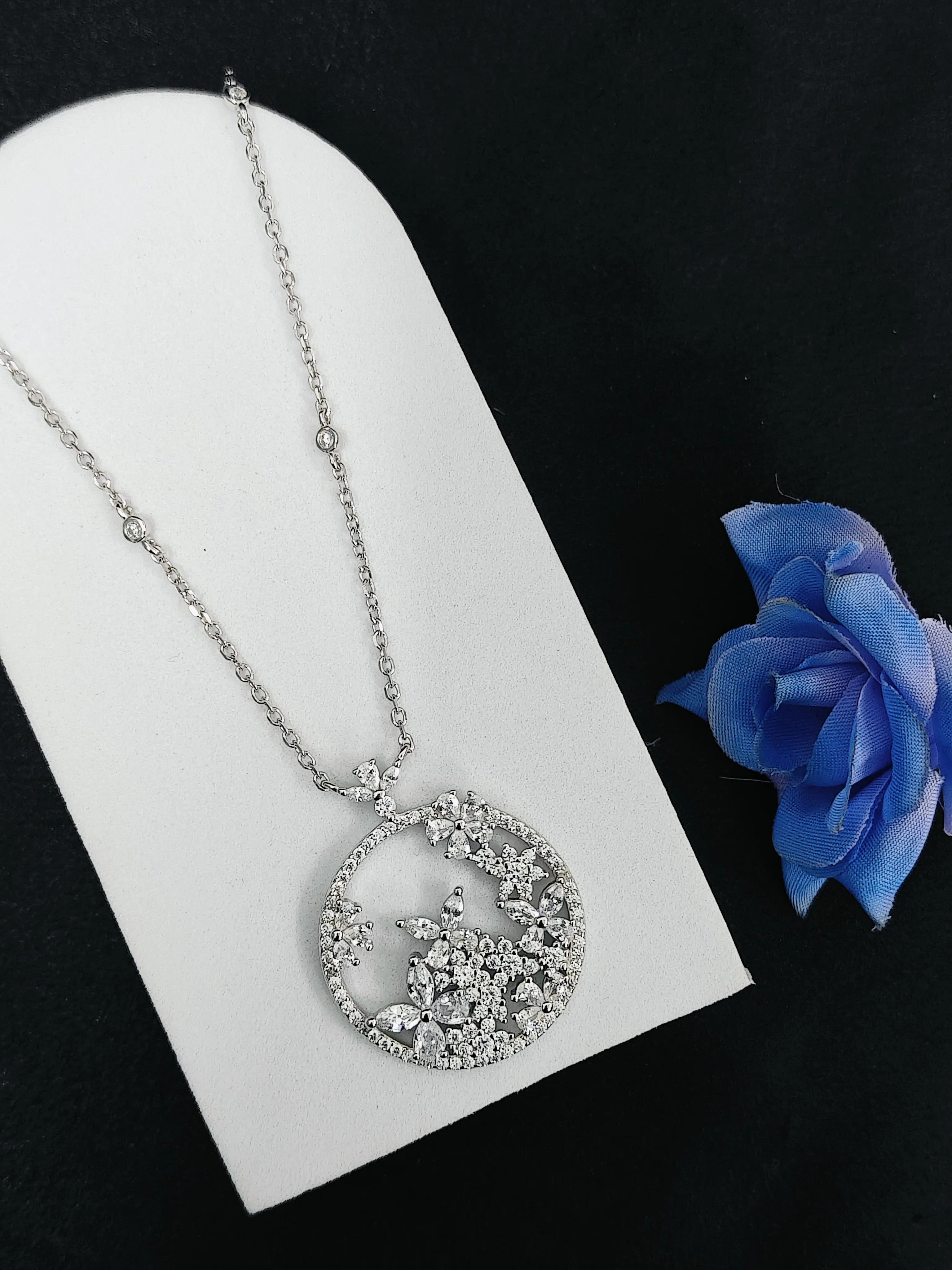Silver necklace with a circular pendant on a white card with a blue rose.