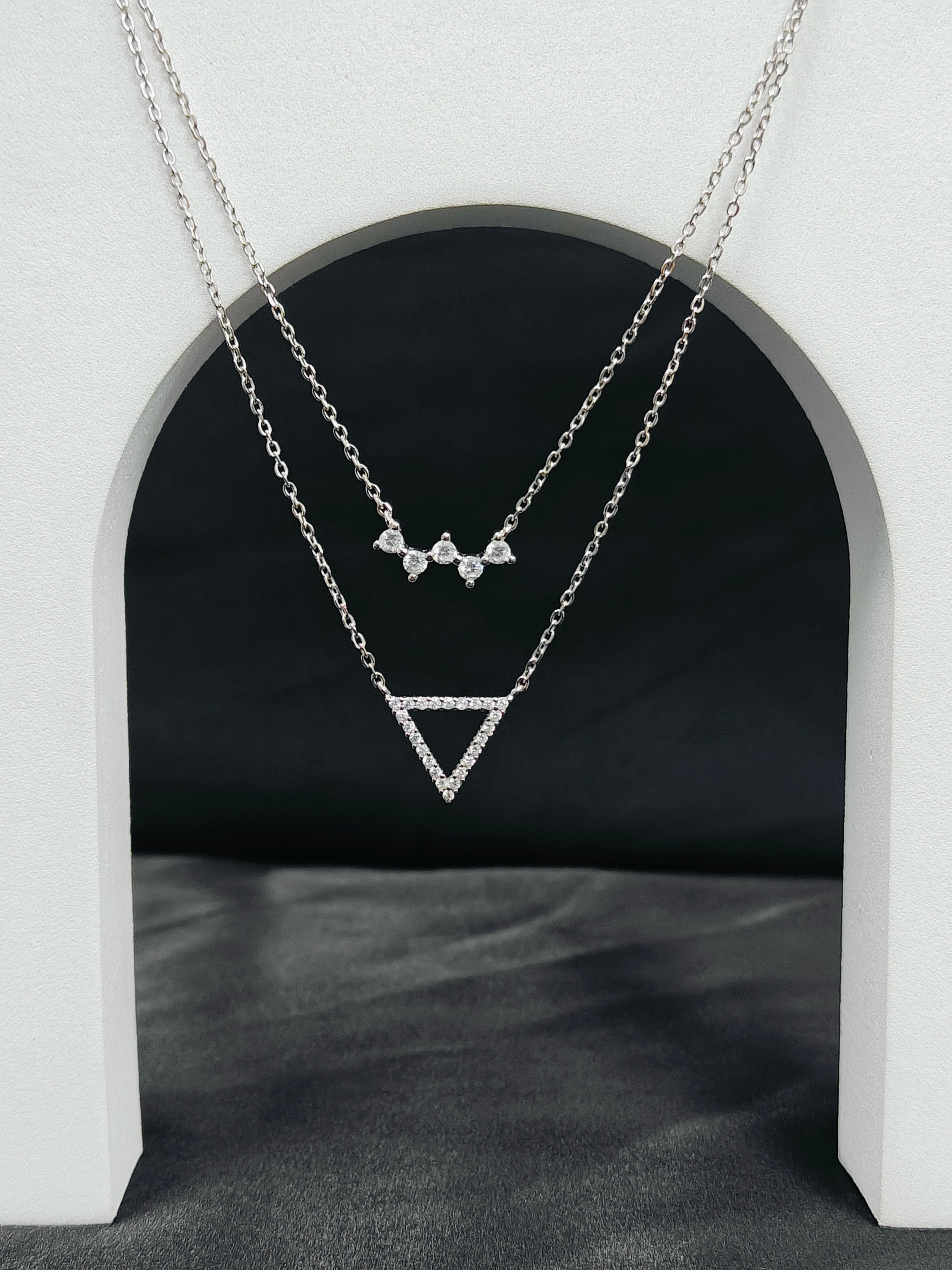 Two silver necklaces with geometric pendants on a dark background