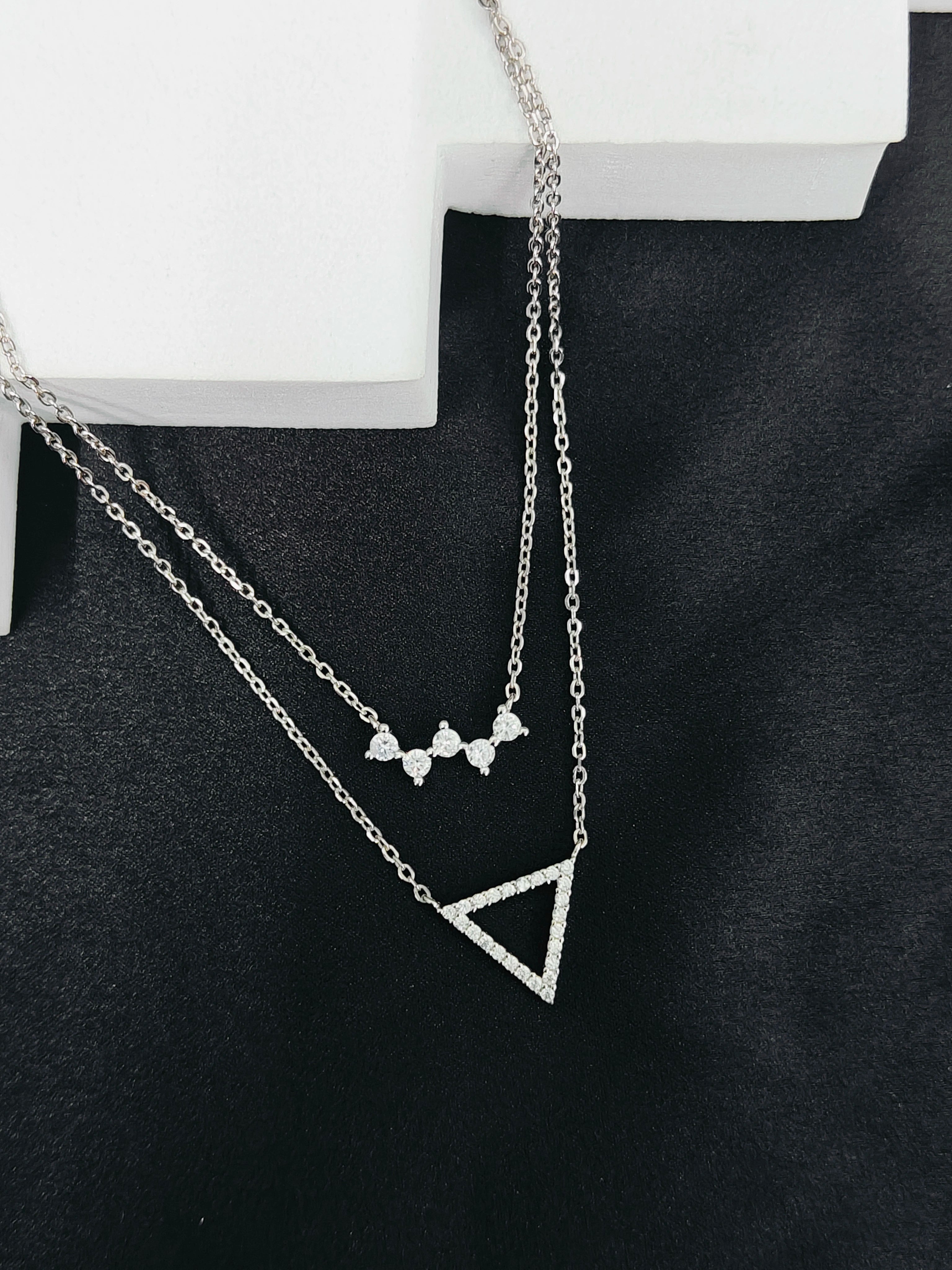 Two silver necklaces with geometric pendants on a black surface.