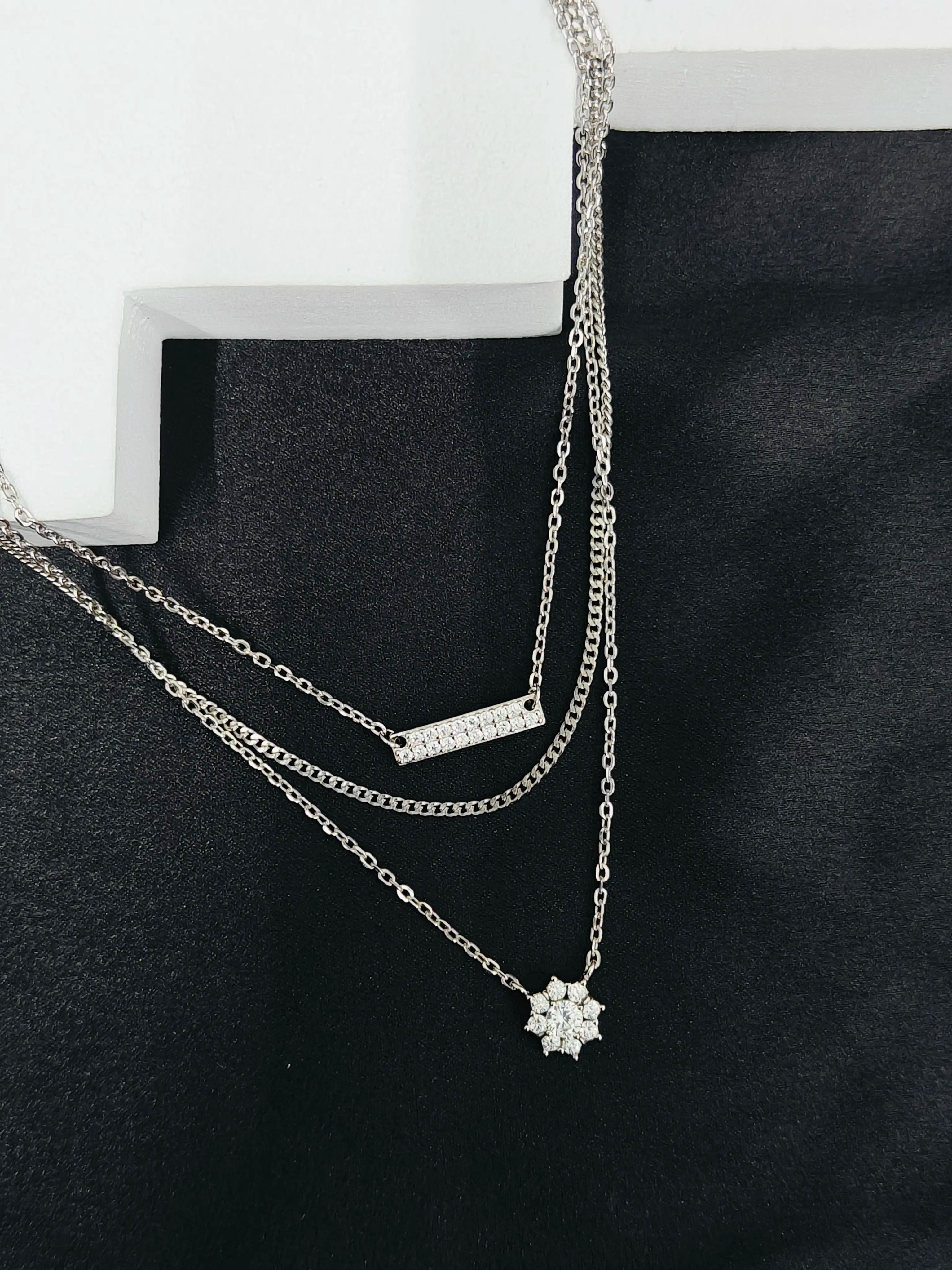 Two silver necklaces on a black stand with a white background