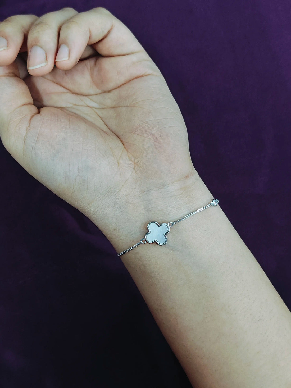 Silver bracelet with a clover charm on a wrist against a purple background