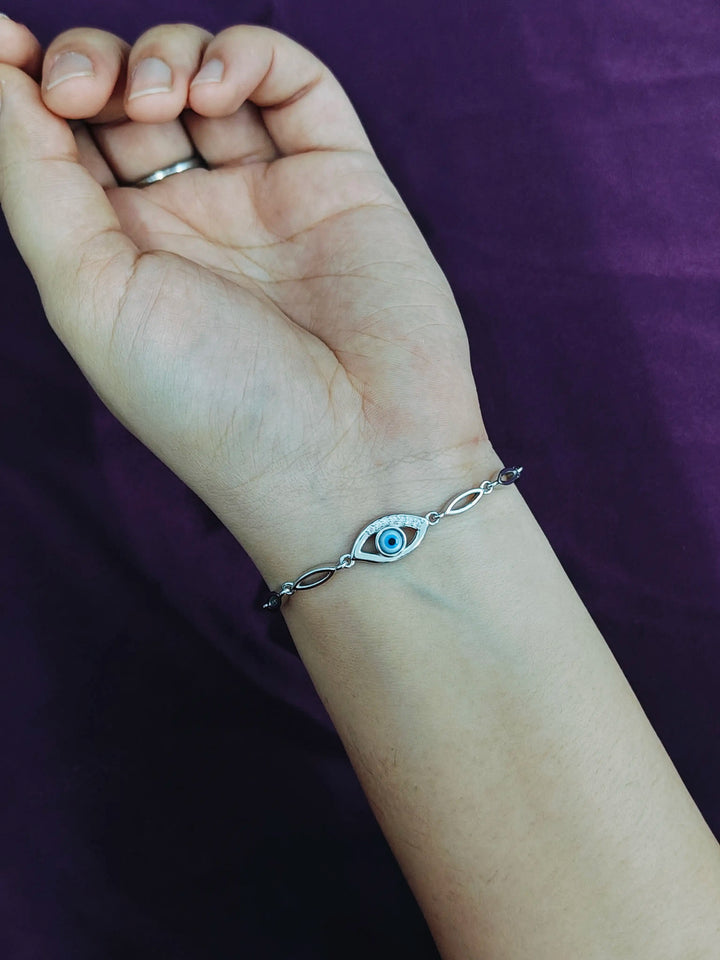 Hand wearing a silver bracelet with an eye design on a purple background