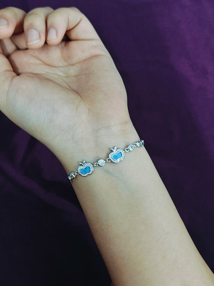 Hand wearing a bracelet with blue heart charms against a purple background