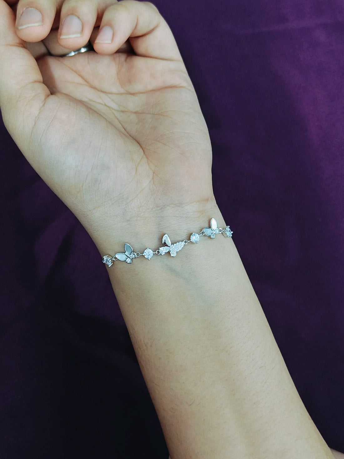 Silver bracelet with butterfly designs on a wrist against a purple background