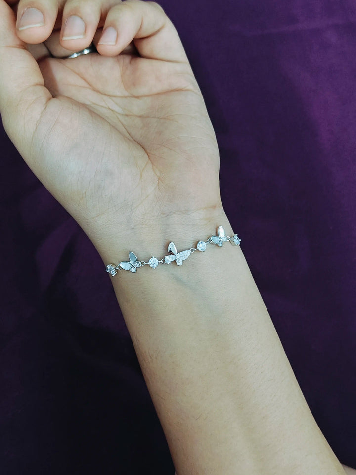 Silver bracelet with butterfly designs on a wrist against a purple background