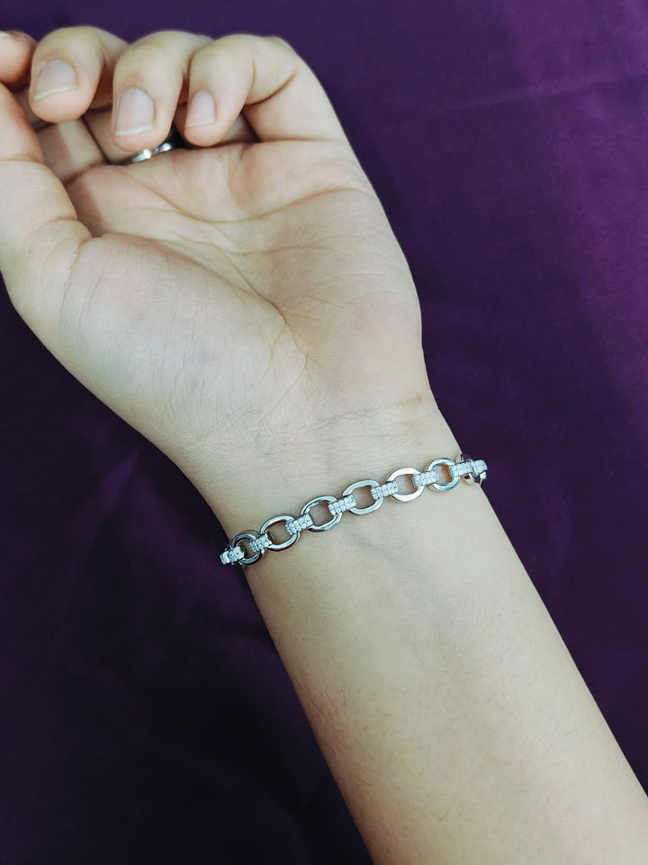 Silver chain bracelet on a wrist with a purple background