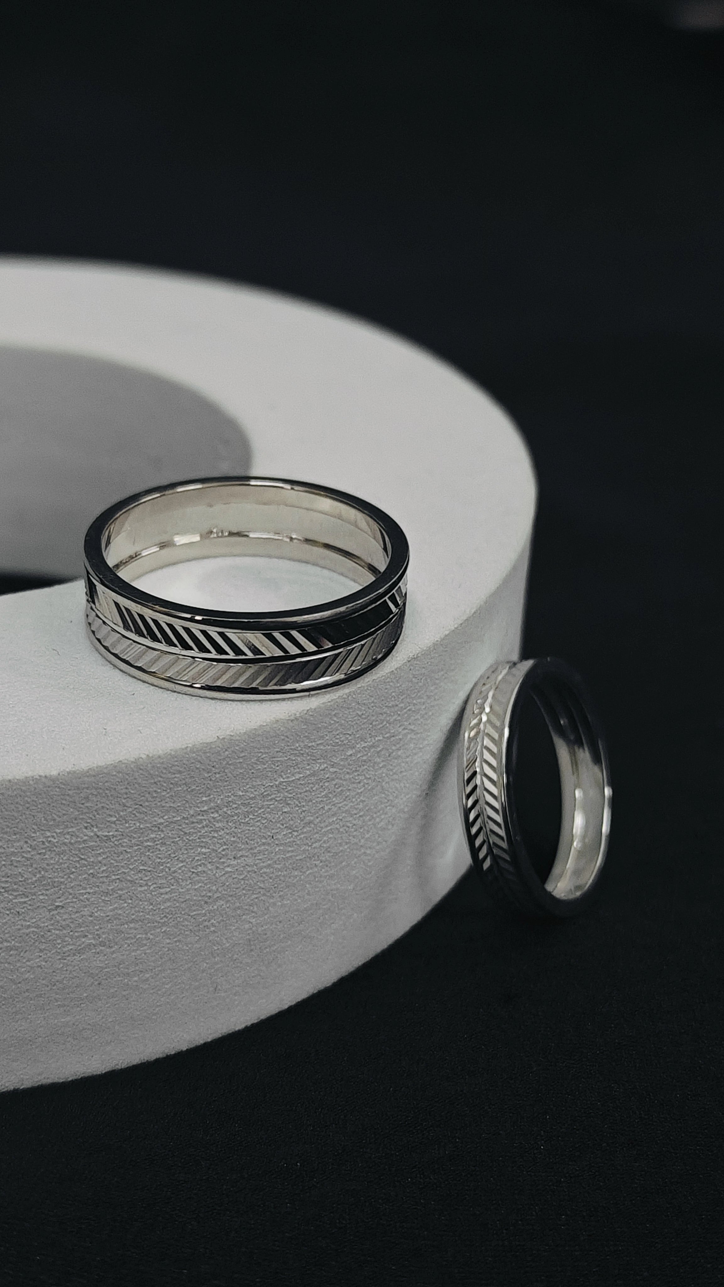 Silver rings with geometric designs on a white cylindrical object against a black background