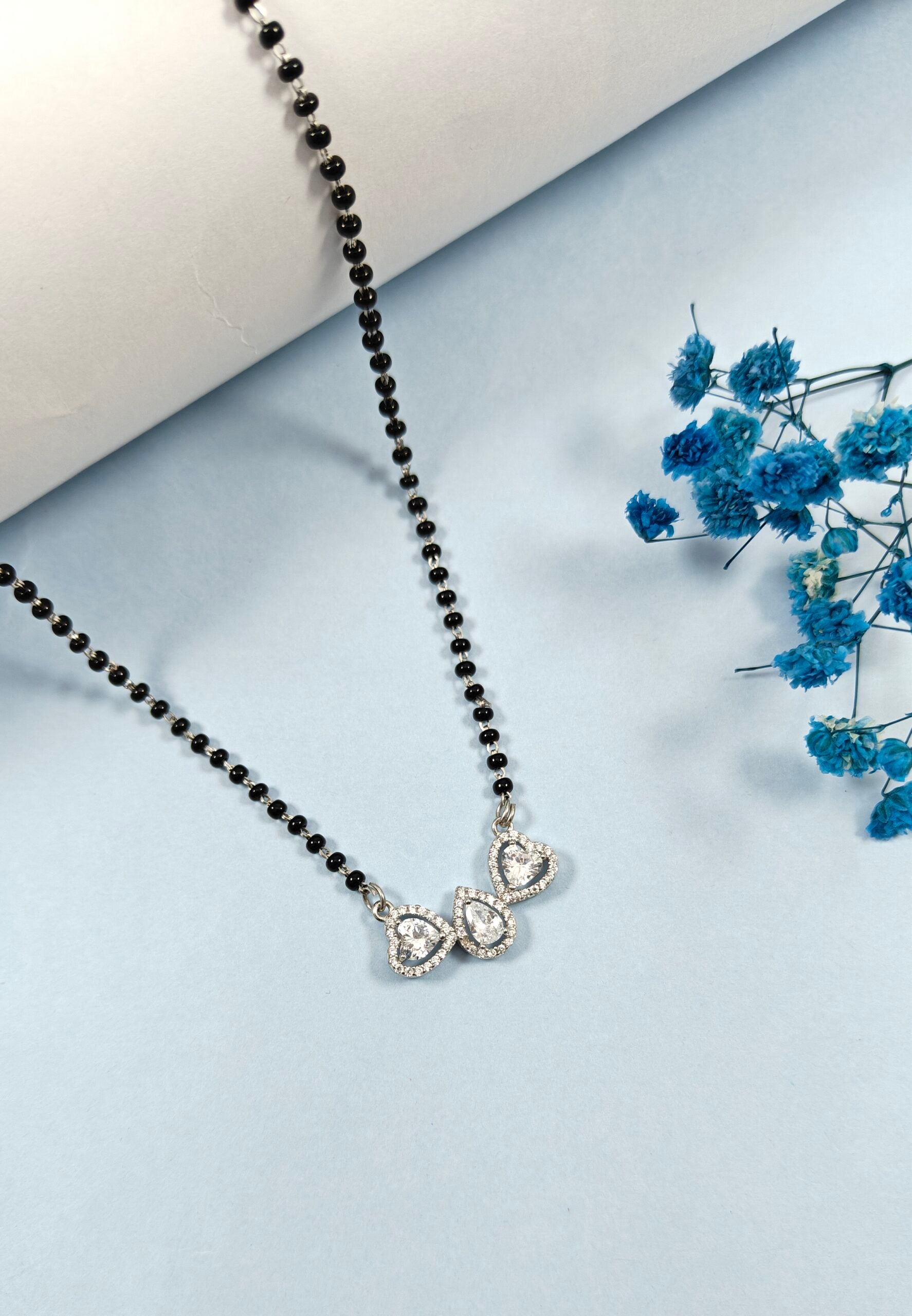 Black beaded necklace with a silver clasp on a light blue surface with blue flowers.