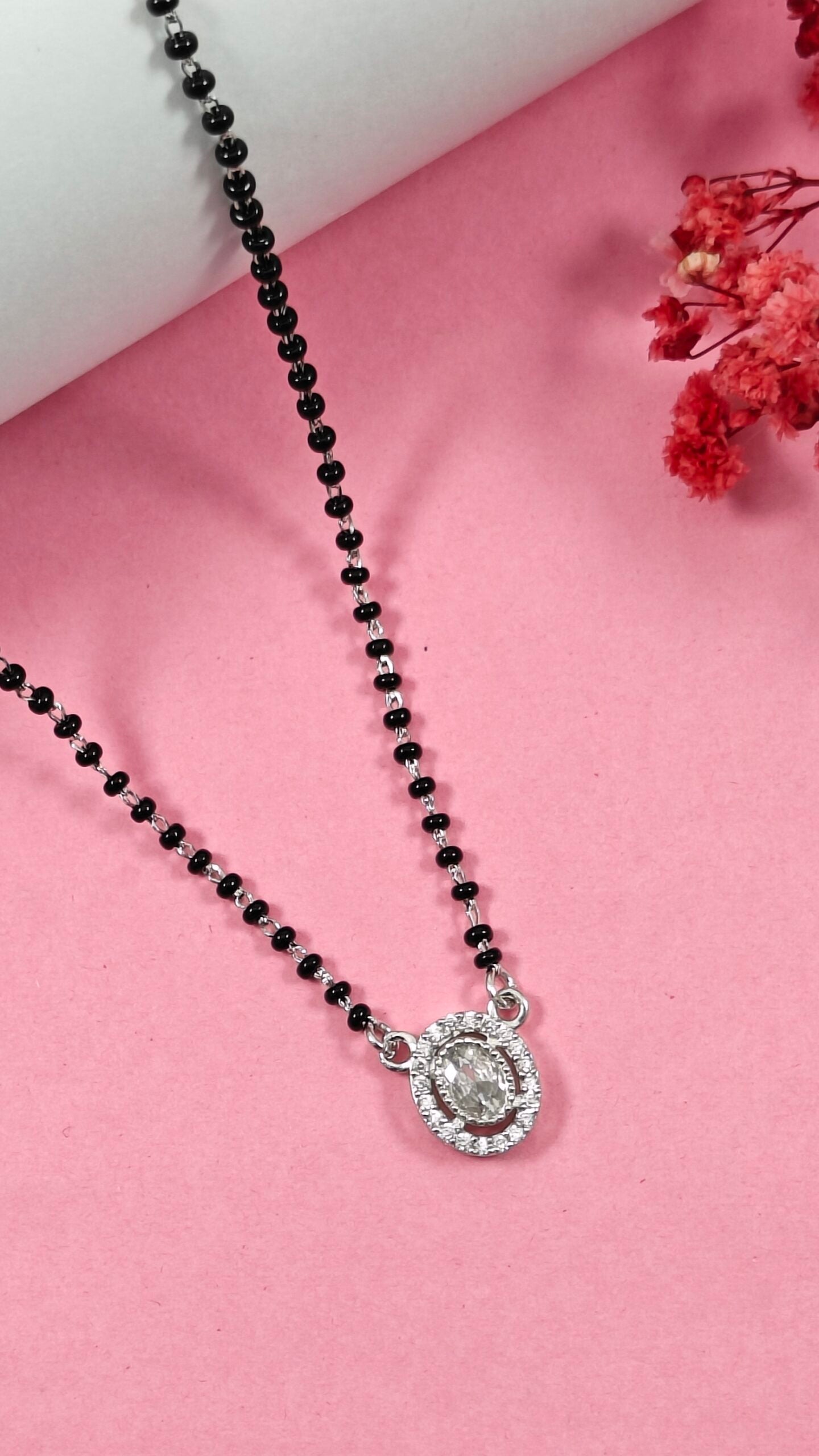 Necklace with black beads and a silver pendant on a pink background
