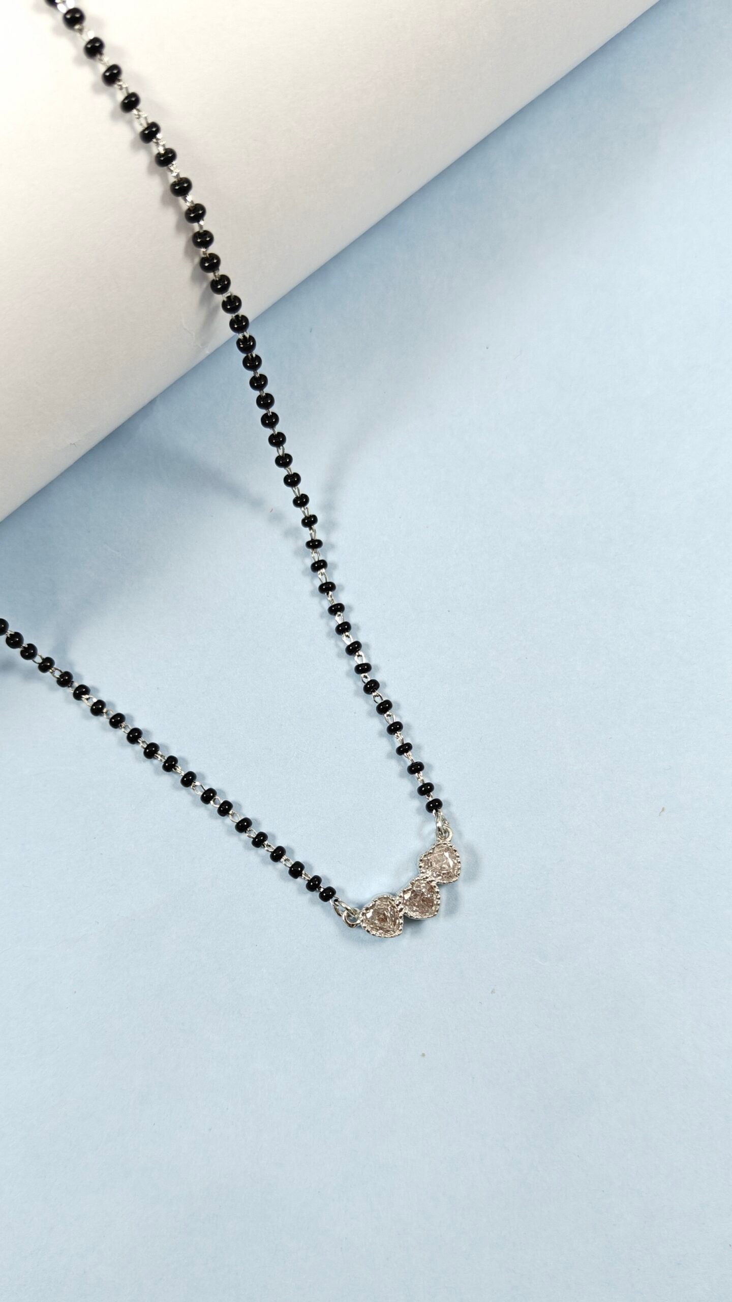Black beaded necklace with a silver clasp on a light blue background