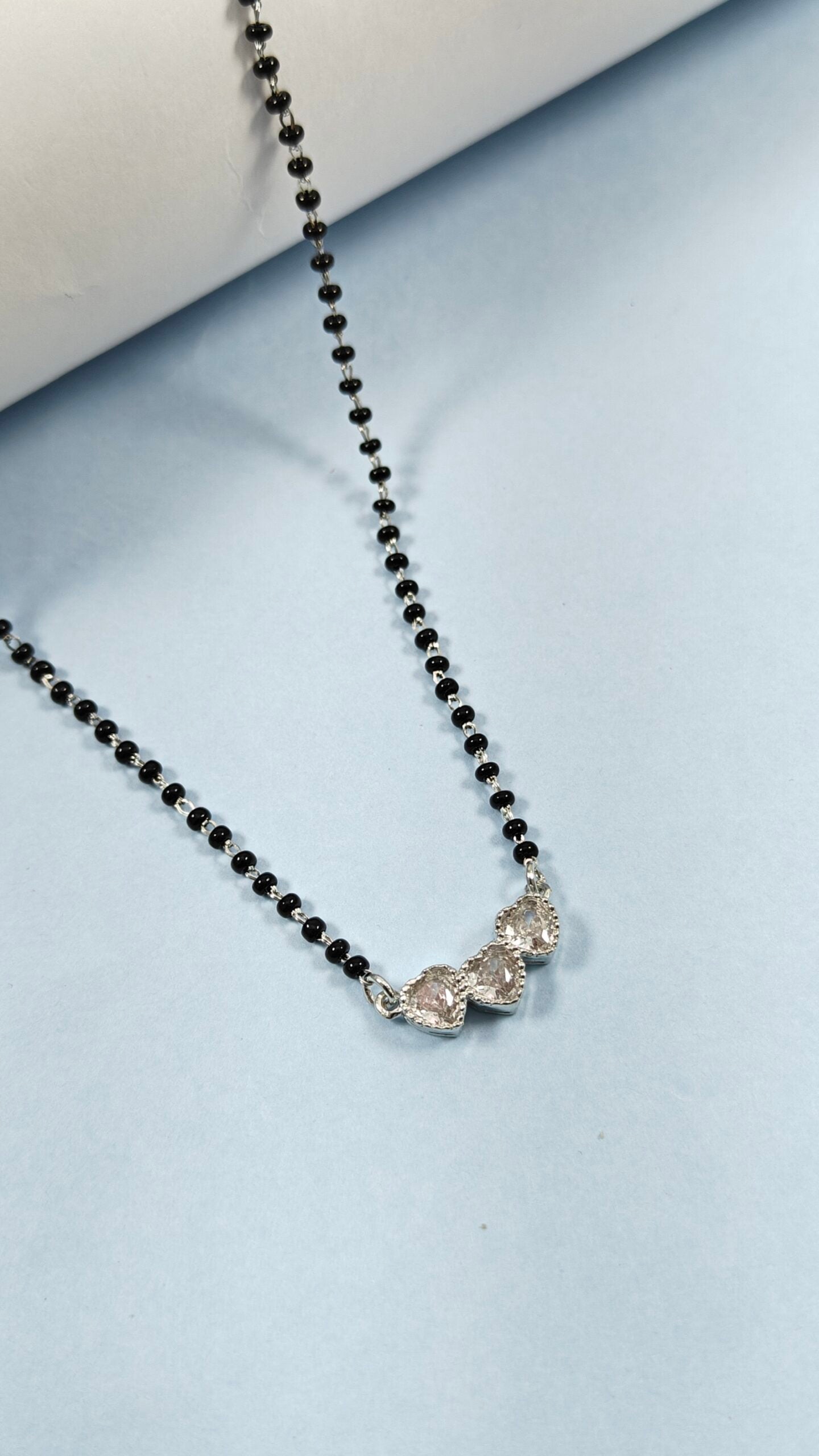 Black beaded necklace with a silver pendant on a light blue background