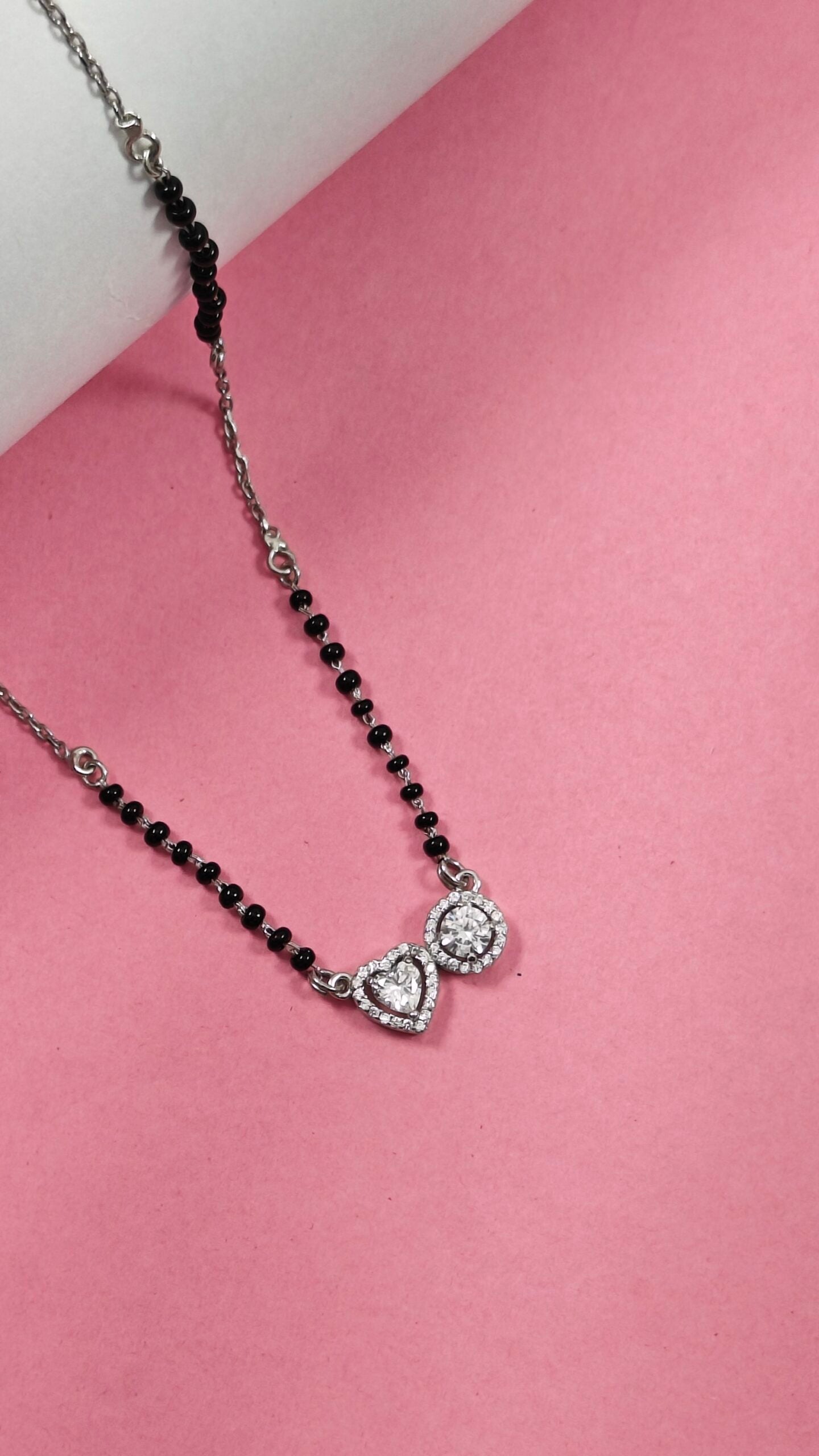Necklace with black beads and heart-shaped pendant on a pink background