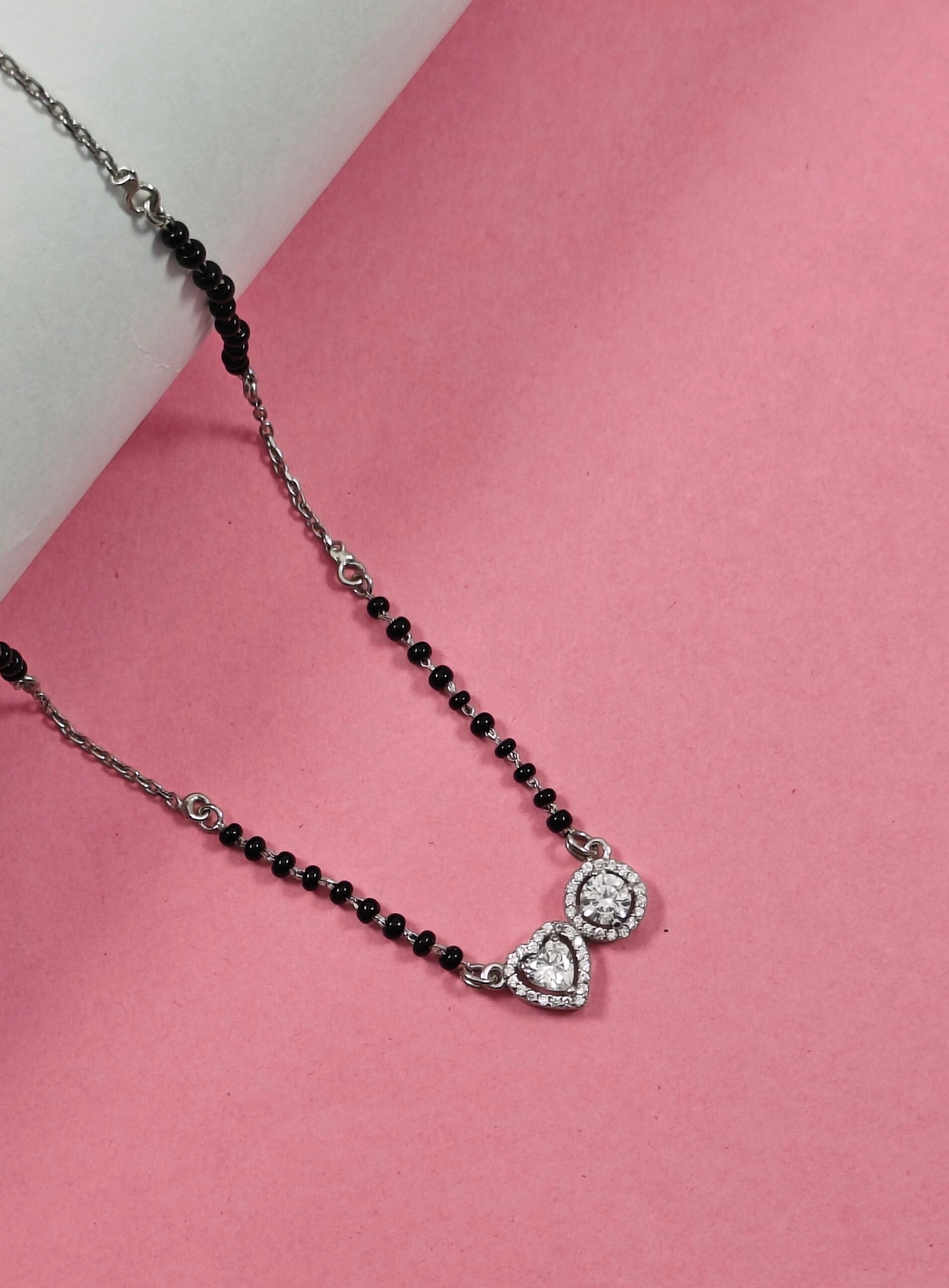 Necklace with black beads and heart-shaped clasp on a pink background