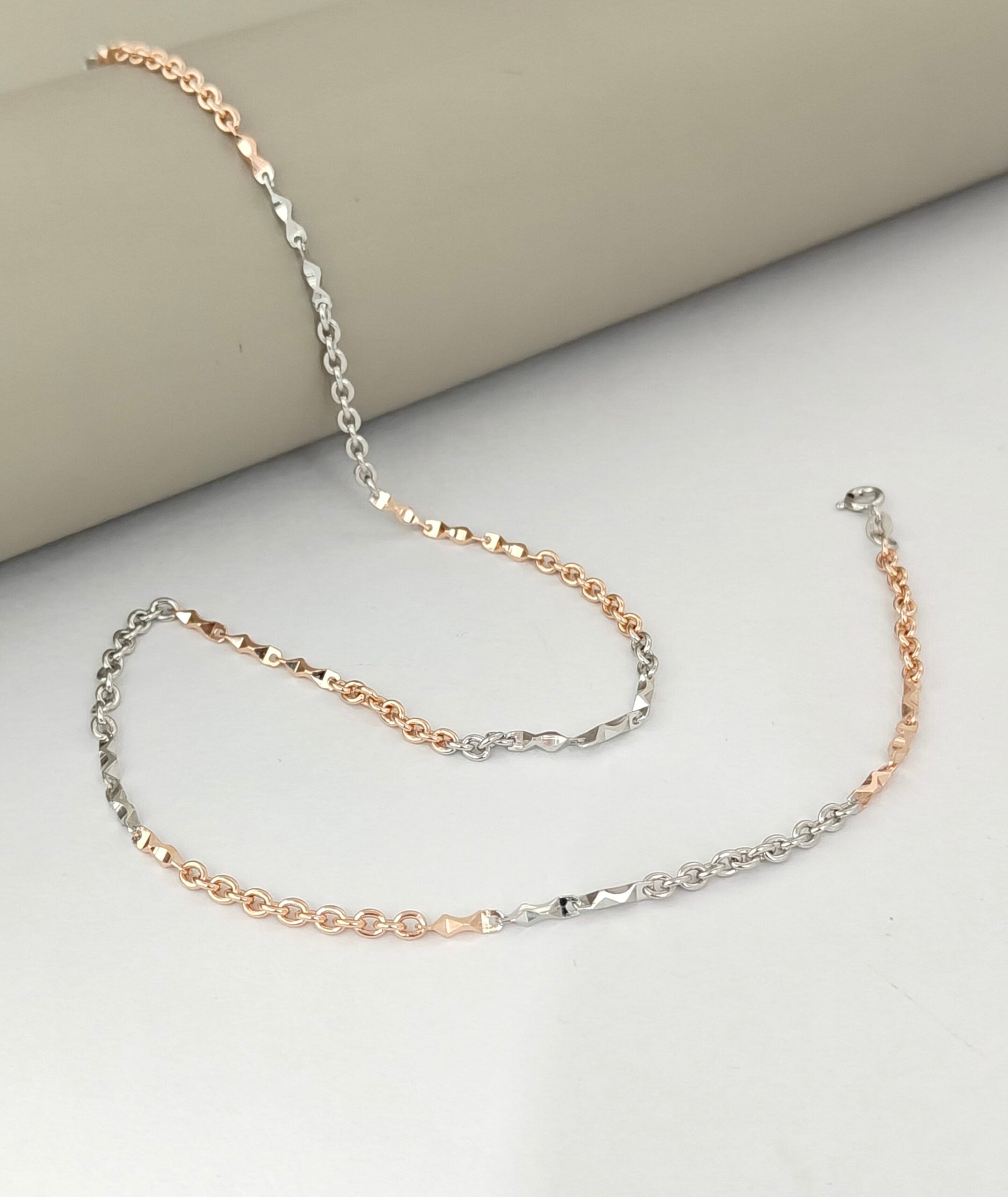 Two gold and silver chain necklaces on a light gray surface.