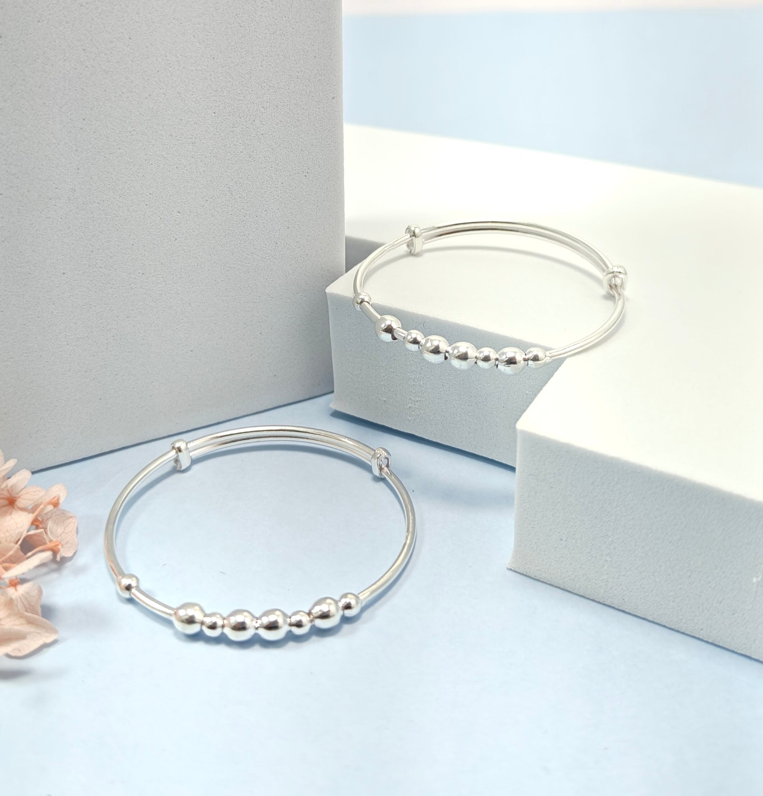 Two silver beaded bracelets on a light blue surface with a white box in the background.