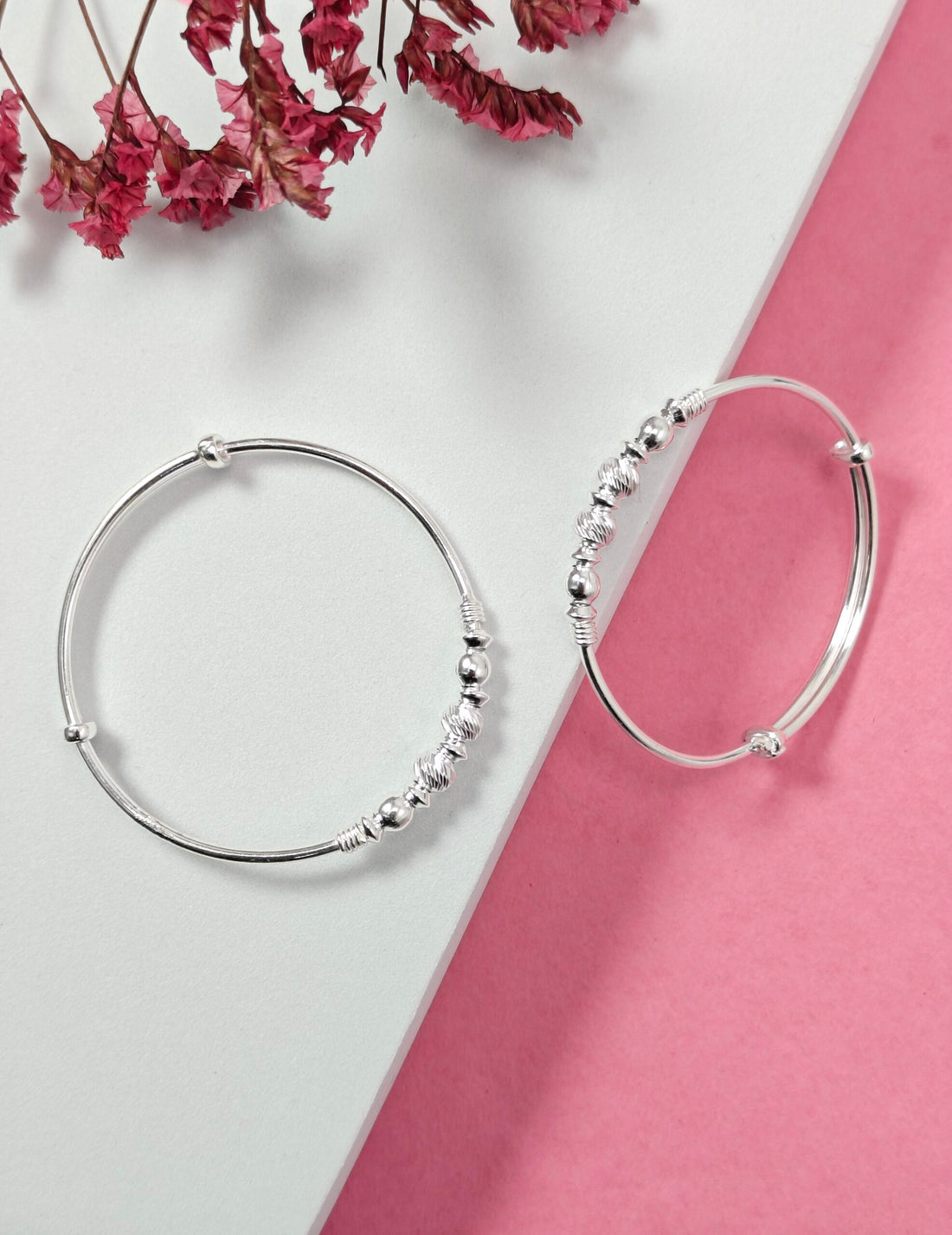 Silver hoop earrings with bead detailing on a pink and white background