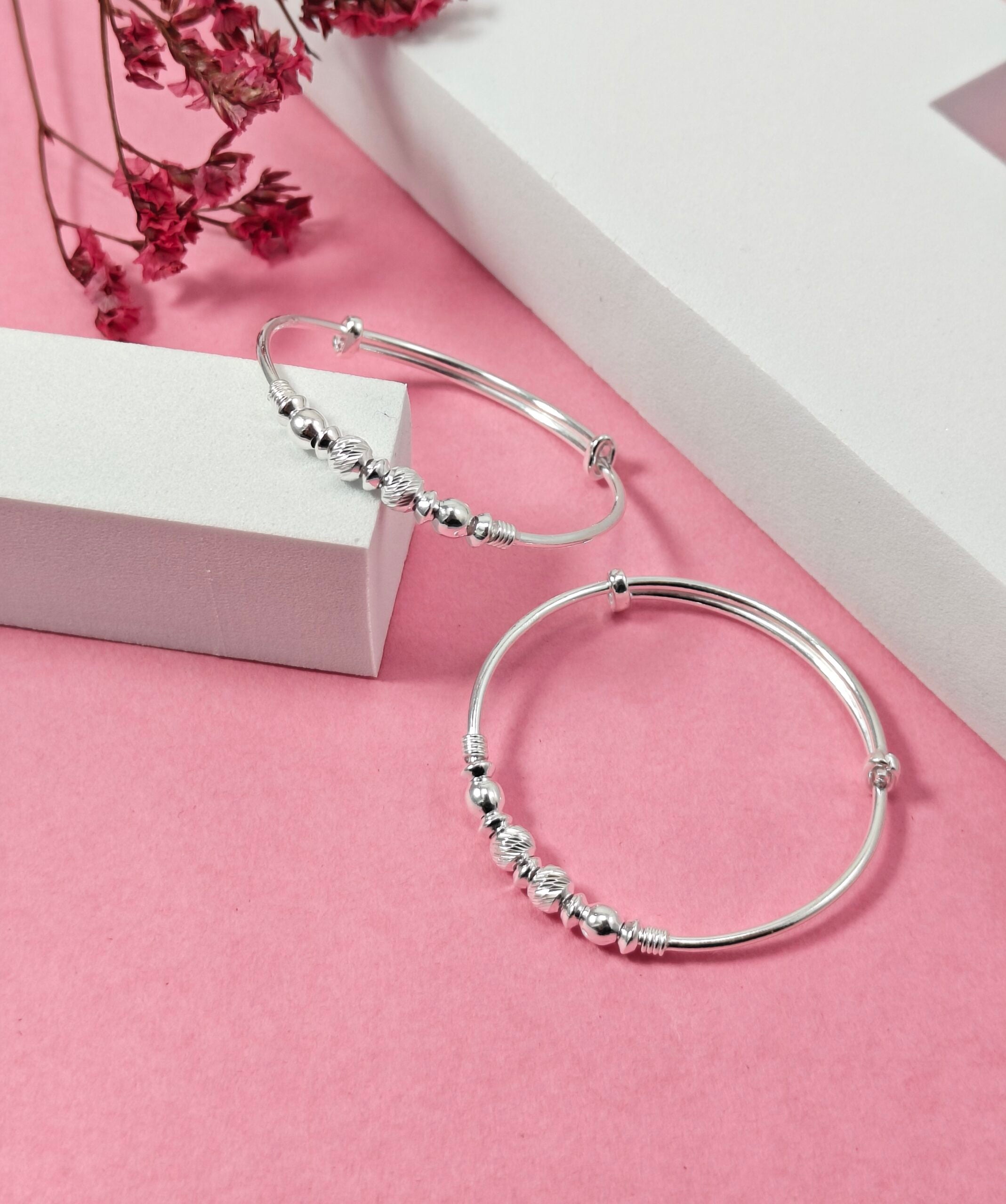 Silver hoop earrings with bead detailing on a pink surface with a white box and red flowers.