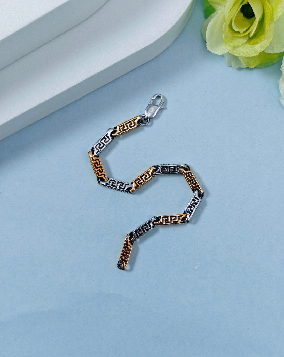 Metallic chain on a light blue surface with a white box and green flowers in the background