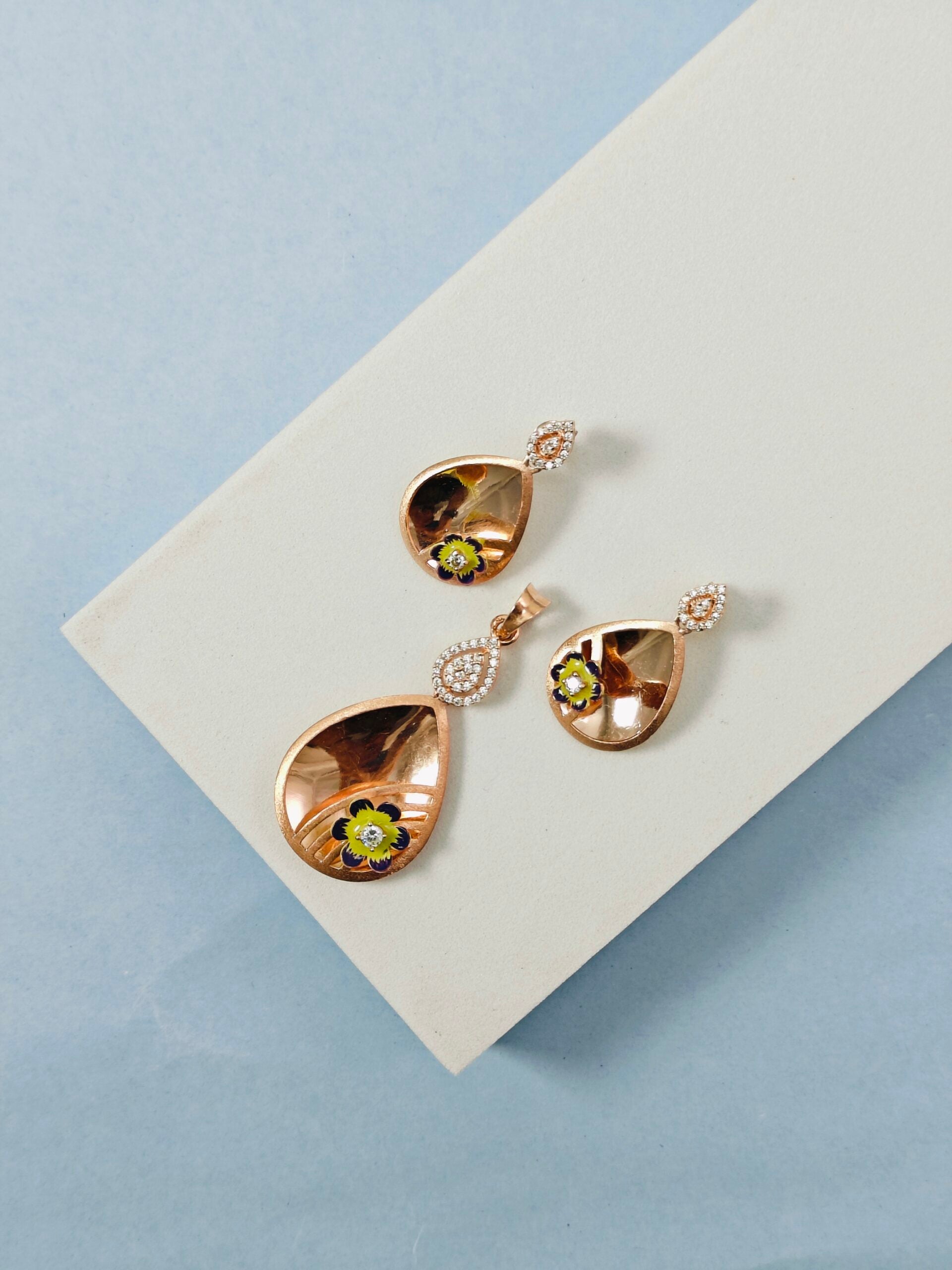 Rose gold earrings with green gemstones on a light gray card against a blue background